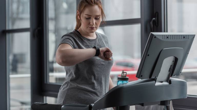 Eine Frau auf einem Laufband schaut auf ihren Fitnesstracker