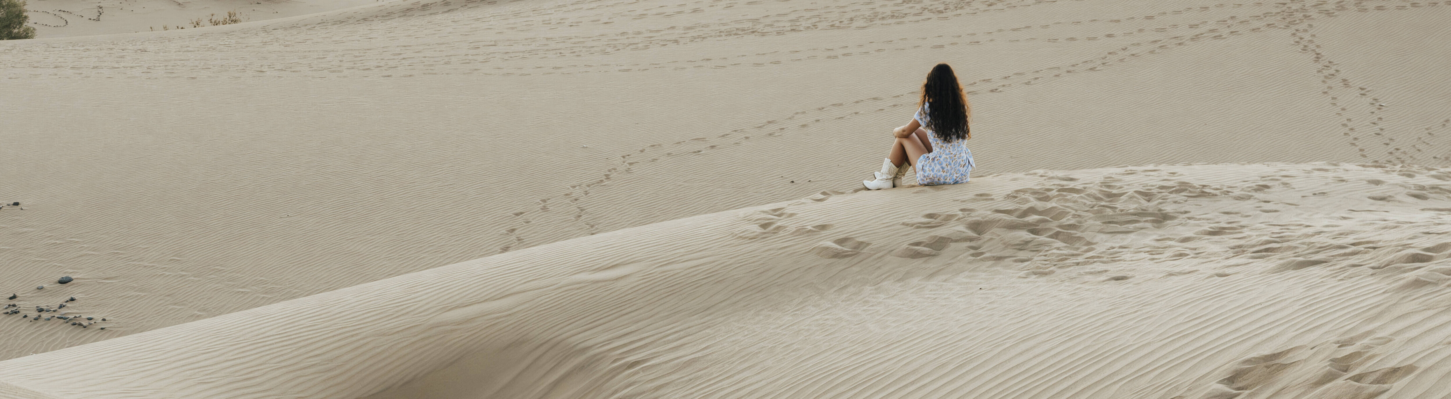 Eine Frau sitzt alleine auf einer Sanddüne in der Wüste