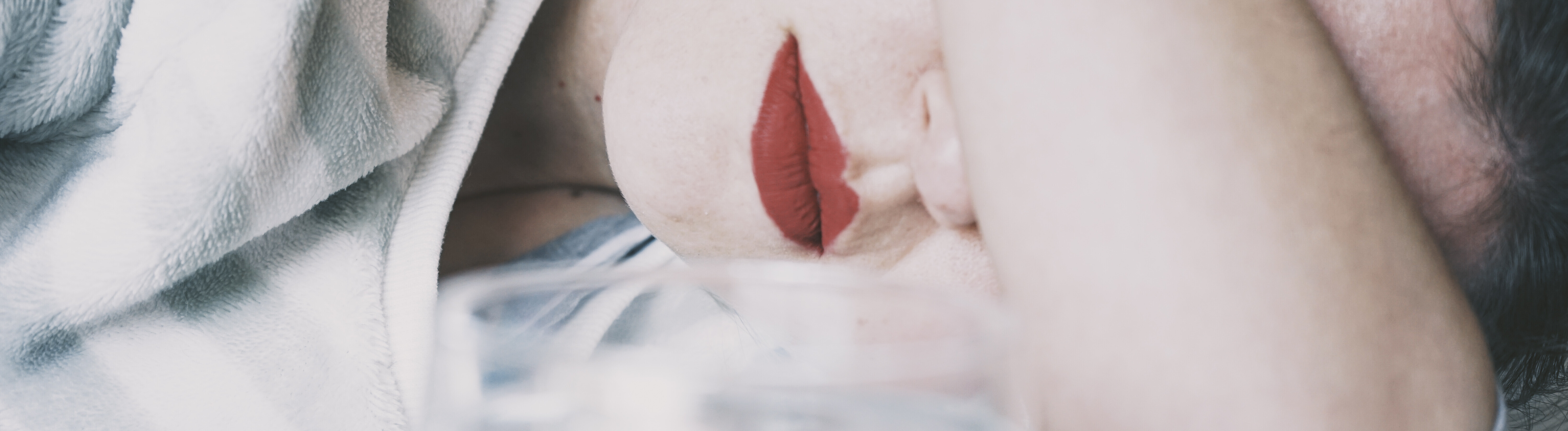 Eine junge Frau verdeckt ihre Augen mit ihrem Arm, vor ihr ein Glas