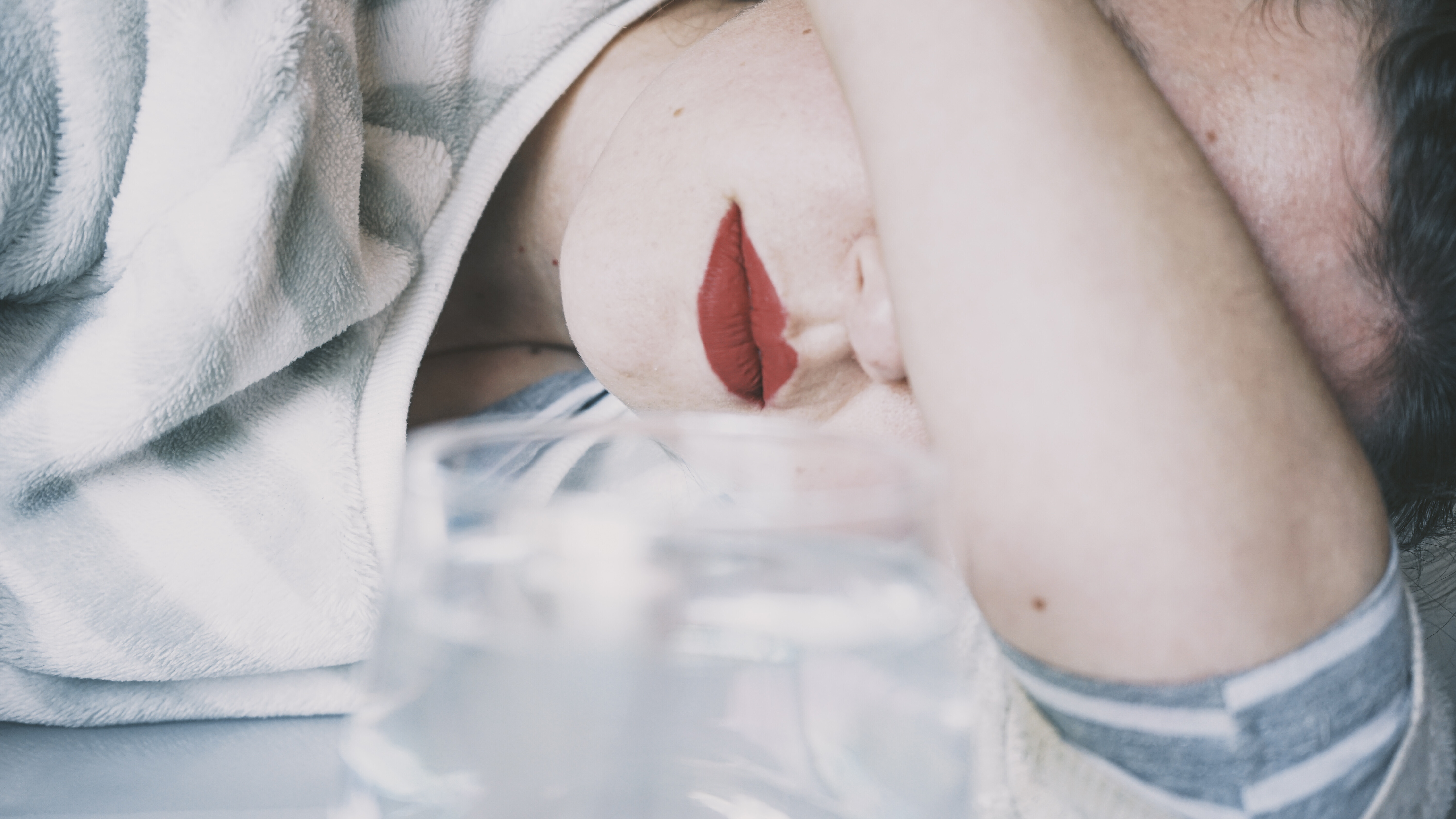 Eine junge Frau verdeckt ihre Augen mit ihrem Arm, vor ihr ein Glas