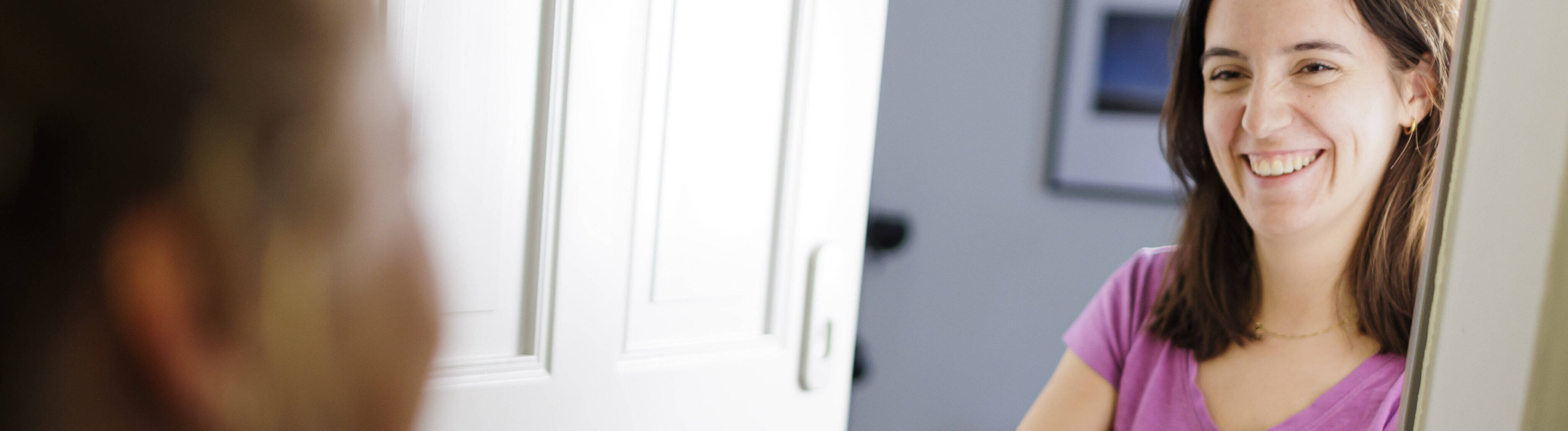 Eine Frau hat ihre Wohnungstür geöffnet. Sie reicht einer anderen Frau im Treppenhaus ein Paket entgegen.