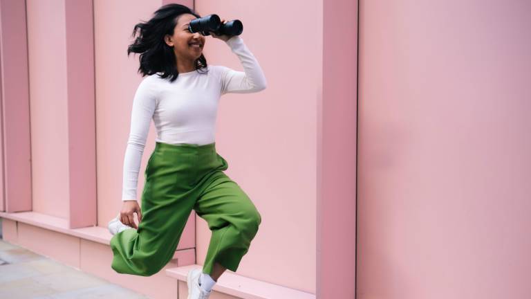 Eine Frau schaut durch ein Fernglas und bewegt sich dabei nach vorne.