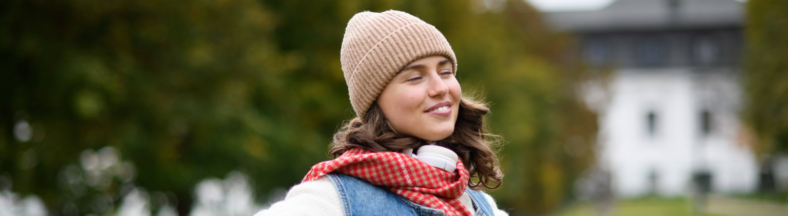 Eine Frau mit Mütze springt über eine Wiese. ihre Augen sind geschlossen