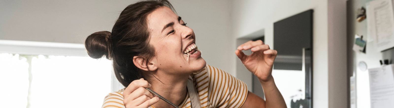 Frau in Küche beugt sich über Kochtopf und probiert etwas daraus