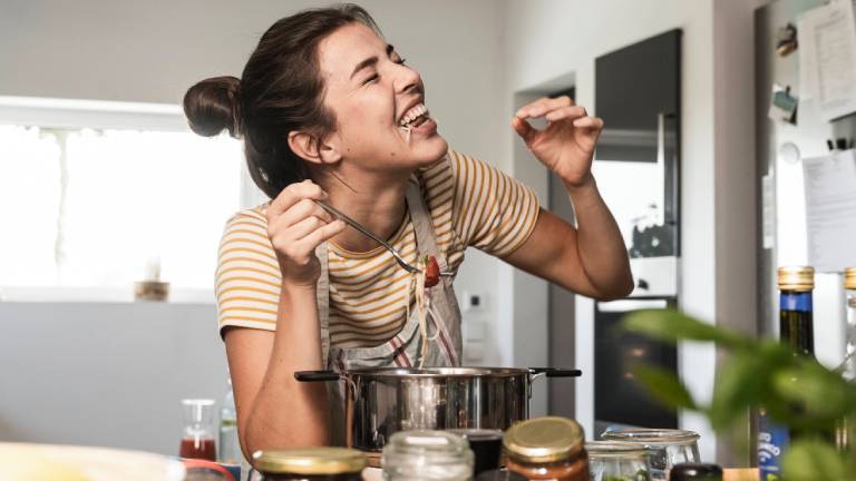 Frau in Küche beugt sich über Kochtopf und probiert etwas daraus