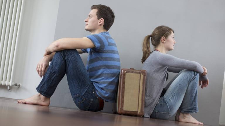Mann und Frau sitzen mit dem Rücken zueinander auf dem Boden, zwischen ihnen steht ein Koffer