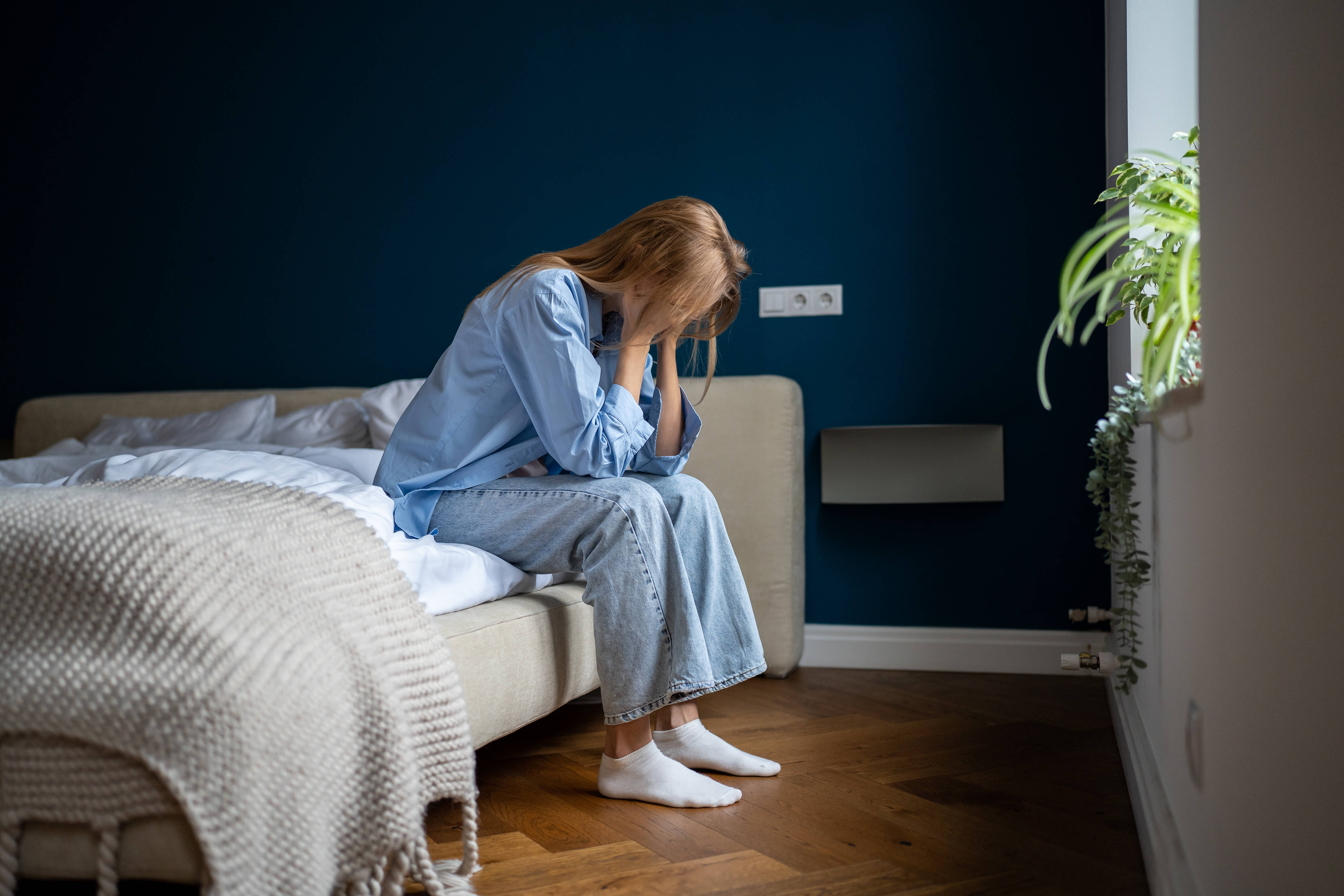 Eine Frau sitzt auf dem Bett im Schlafzimmer und stützt ihr Gesicht in die Hände