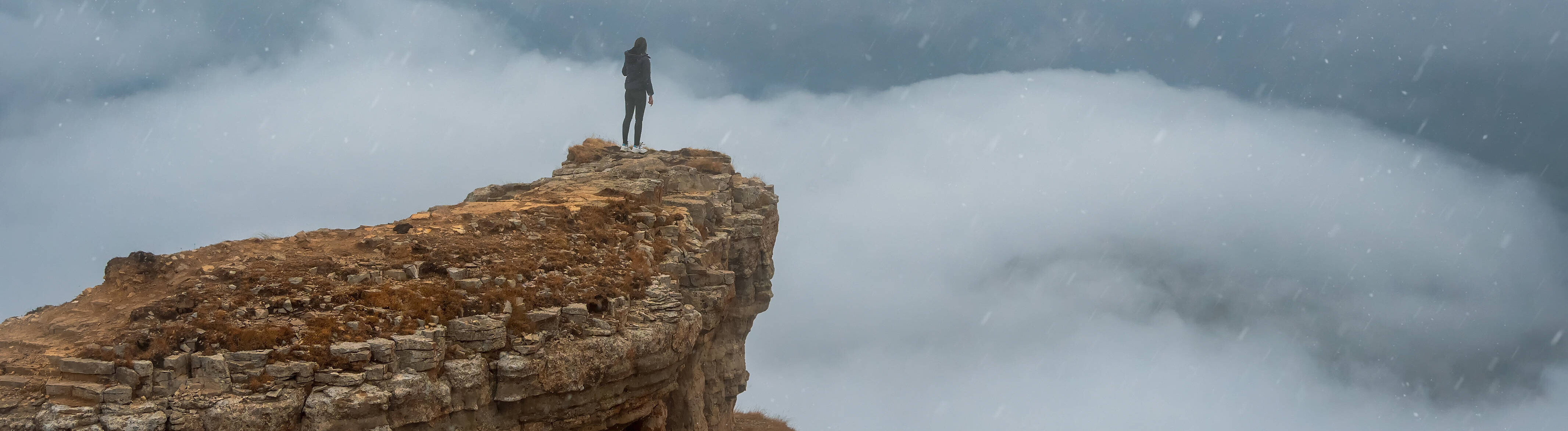 Eine Person steht an einem Klippenrand auf einem Berg
