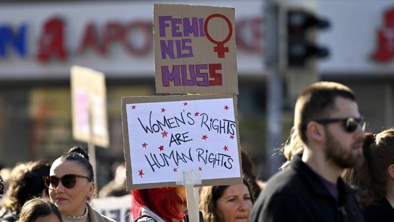 Auf einer Demo zum Weltfrauentag hält eine Teilnehmerin zwei Schilder in die Höhe, auf dem unteren steht "Women’s rights are human rights", auf dem oberen Feminismus mit zwei s (Frankfurt, 08.03.2025)