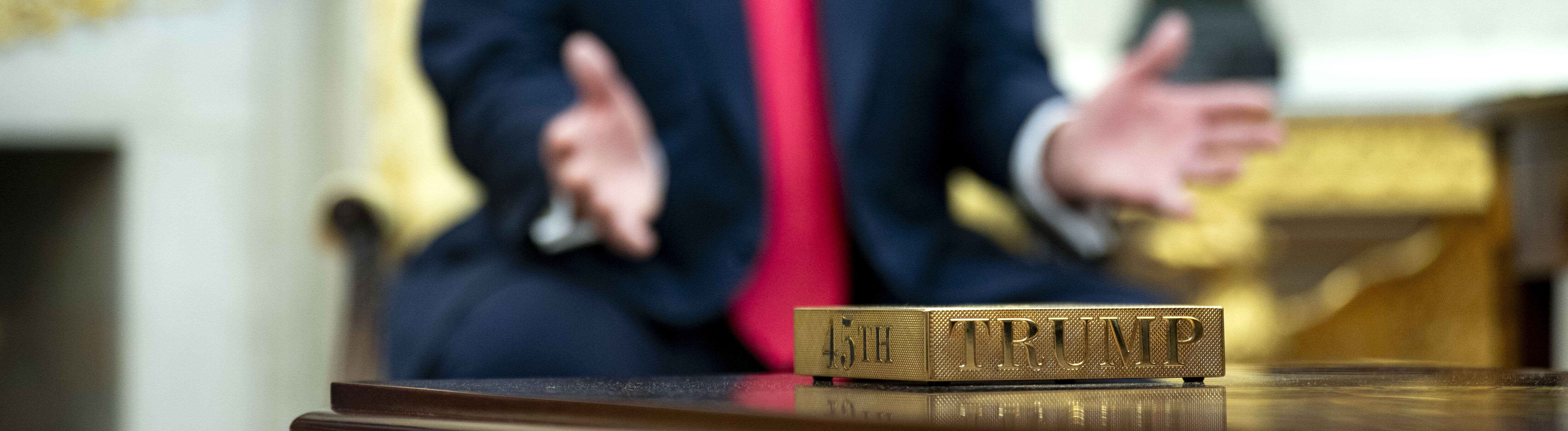 Vergoldeter Untersetzer mit der Aufschrift "45th" und "Trump". Im Hintergrund US-präsident Donald Trump