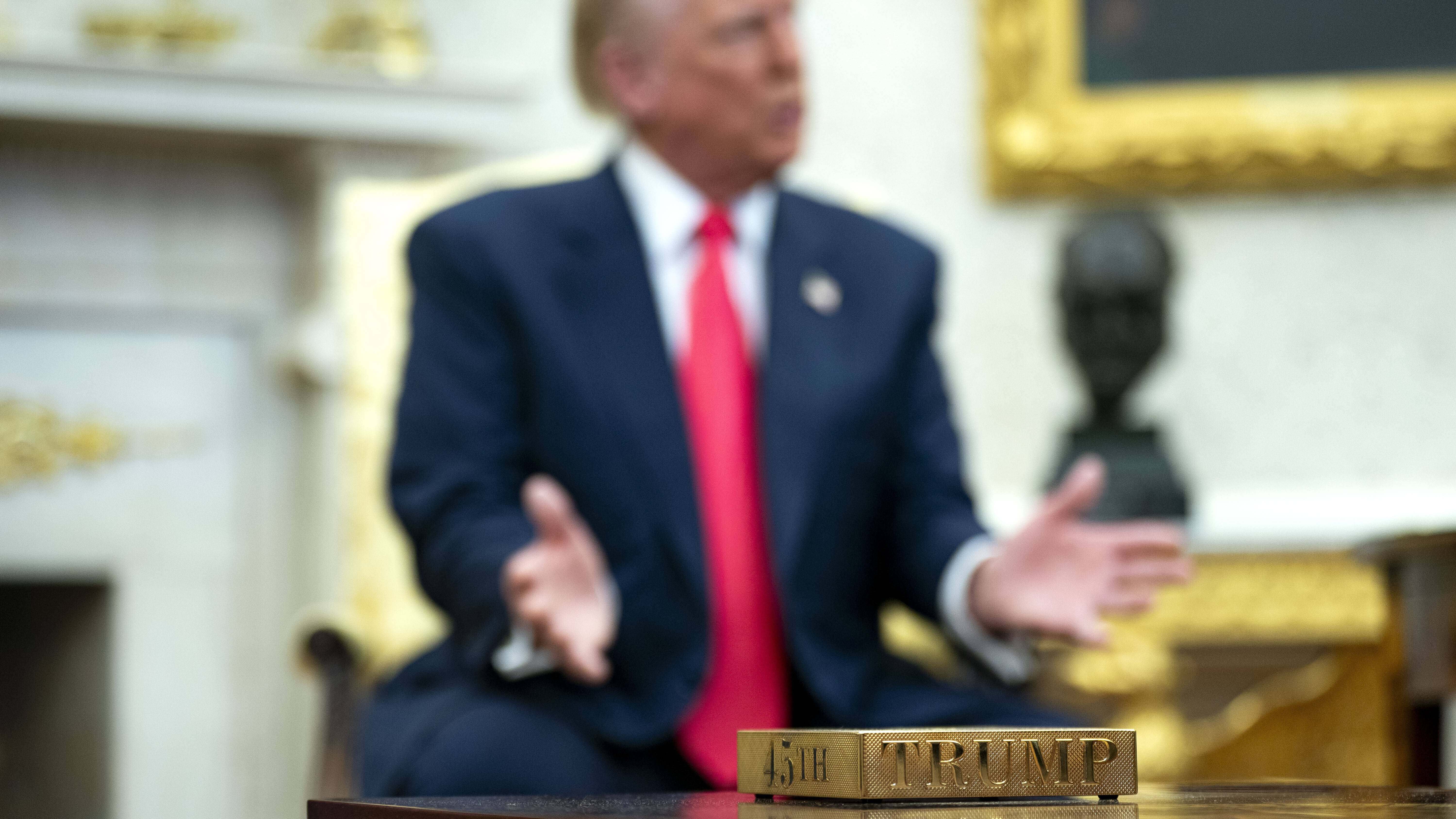 Vergoldeter Untersetzer mit der Aufschrift "45th" und "Trump". Im Hintergrund US-präsident Donald Trump