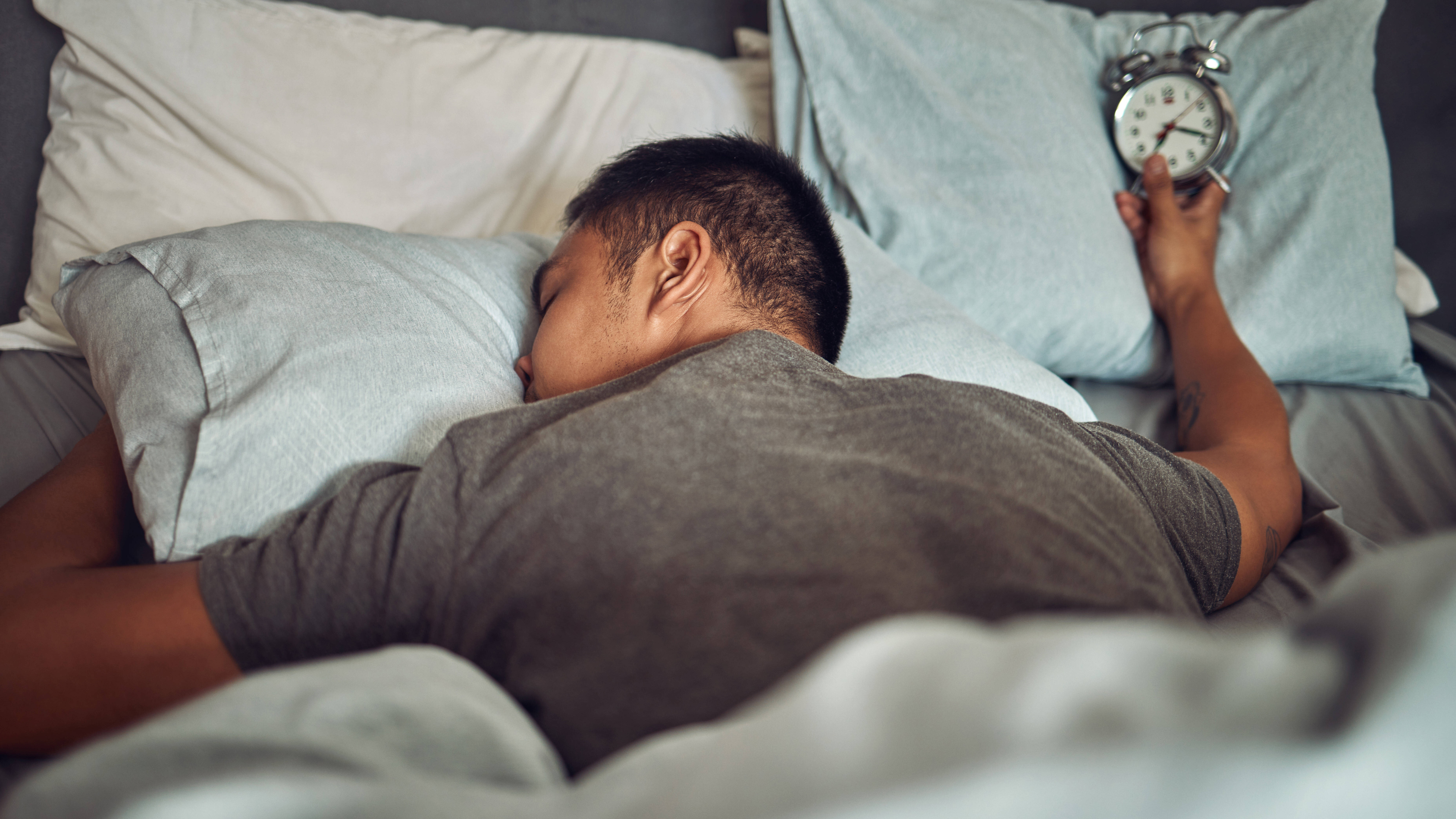 Mann mit Wecker liegt platt im Bett