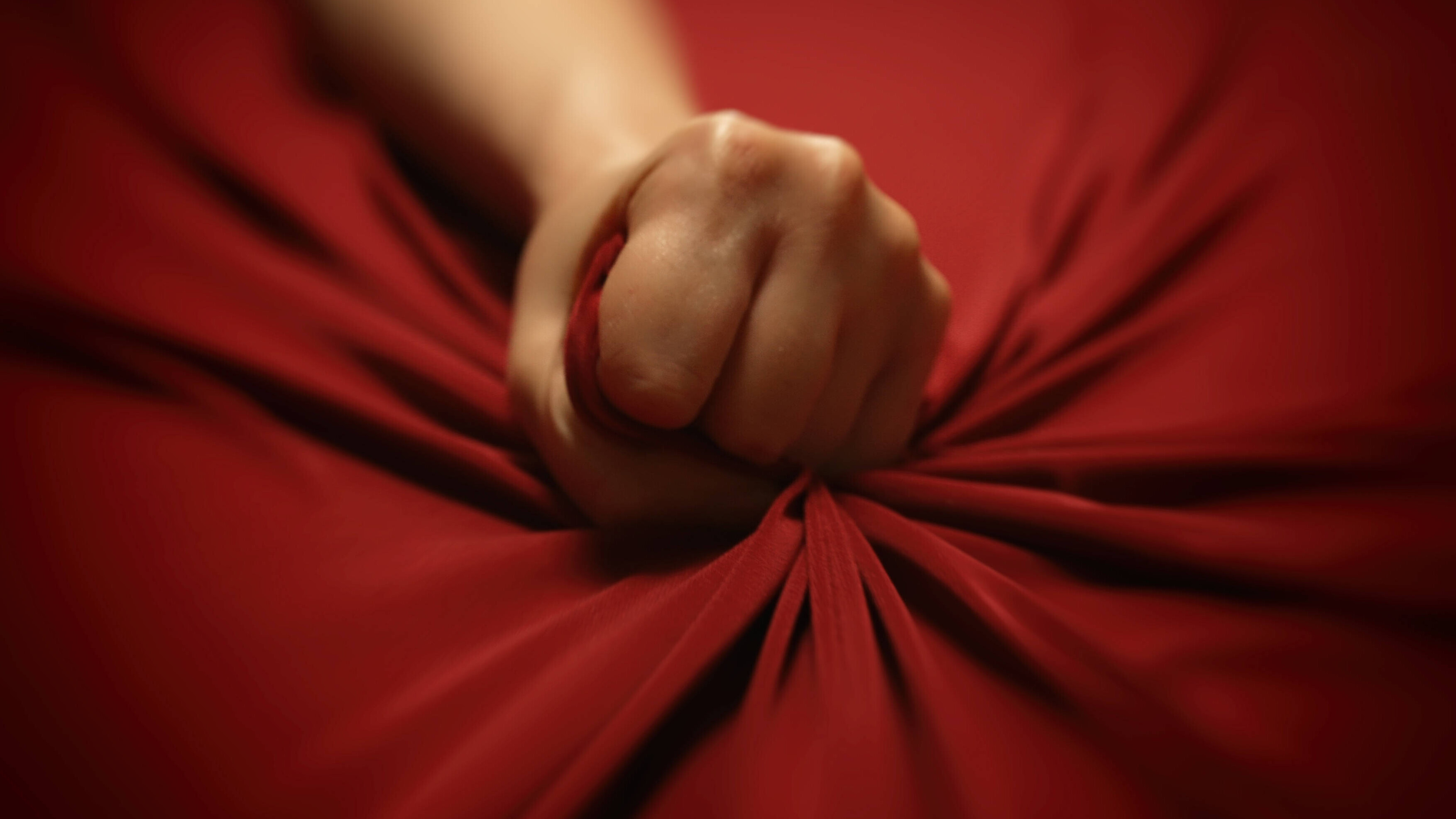 Die Hand einer Frau krallt sich leidenschaftlich in ein rotes Bettlaken.