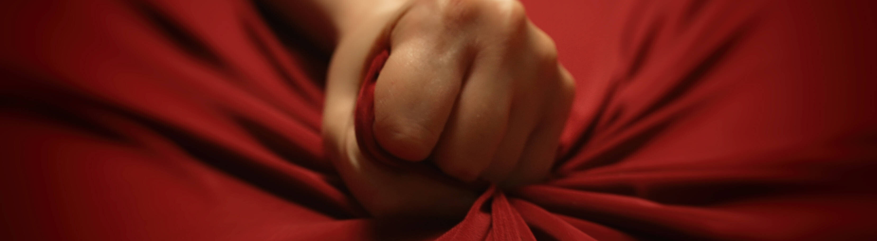 Die Hand einer Frau krallt sich leidenschaftlich in ein rotes Bettlaken.