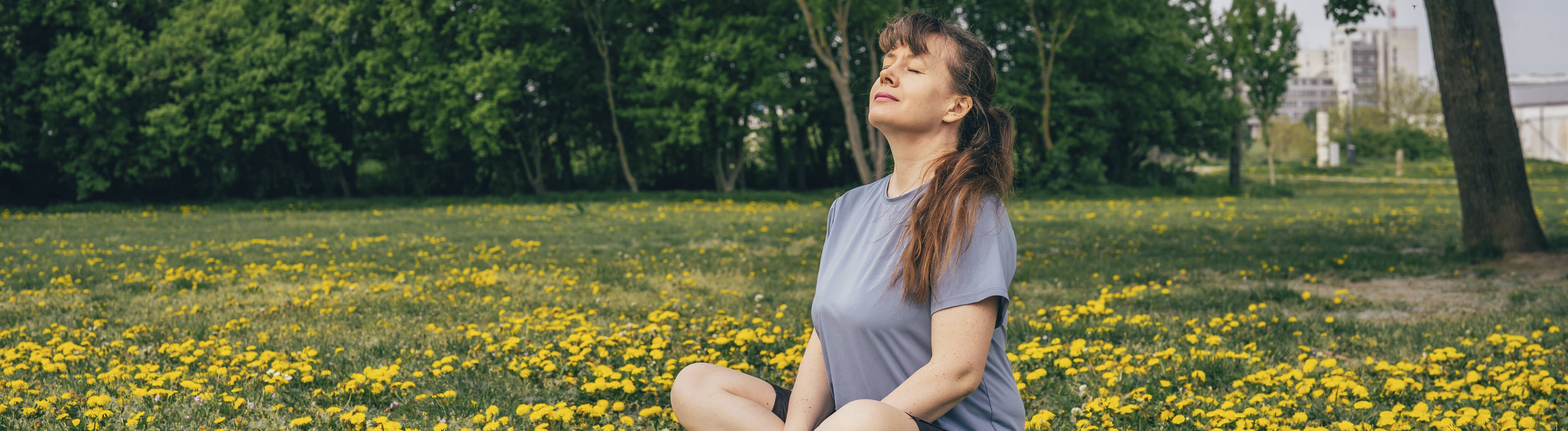 Eine Frau sitzt auf einer Wiese und hat die Augen geschlossen