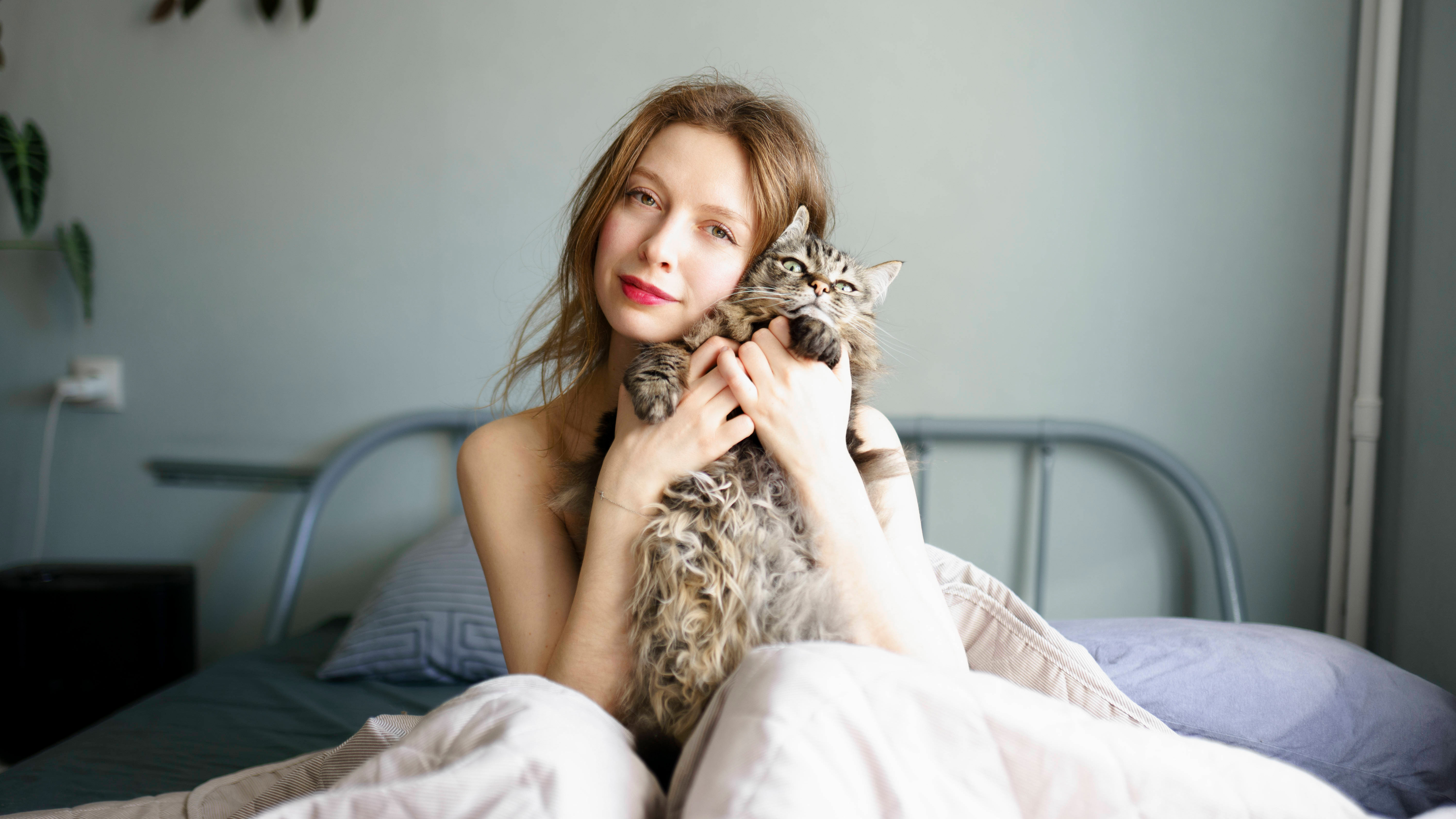 Frau mit Katze auf dem Arm im Bett.