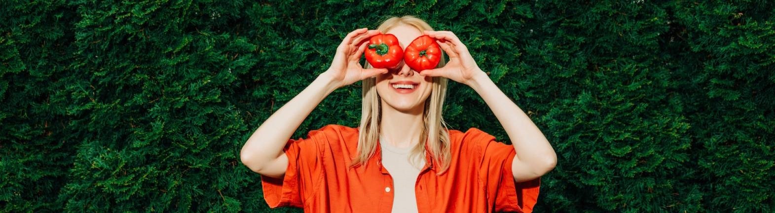 Eine Frau hält sich eine Paprika und eine Tomate vor die Augen