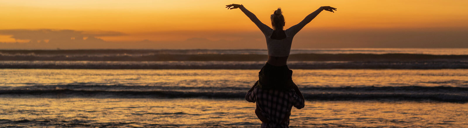 Ein Mann trägt eine Frau an einem Strand auf Bali auf seinen Schultern