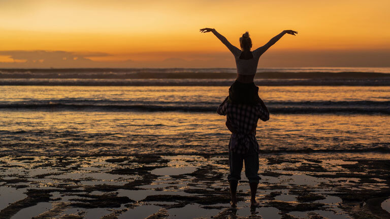 Ein Mann trägt eine Frau an einem Strand auf Bali auf seinen Schultern