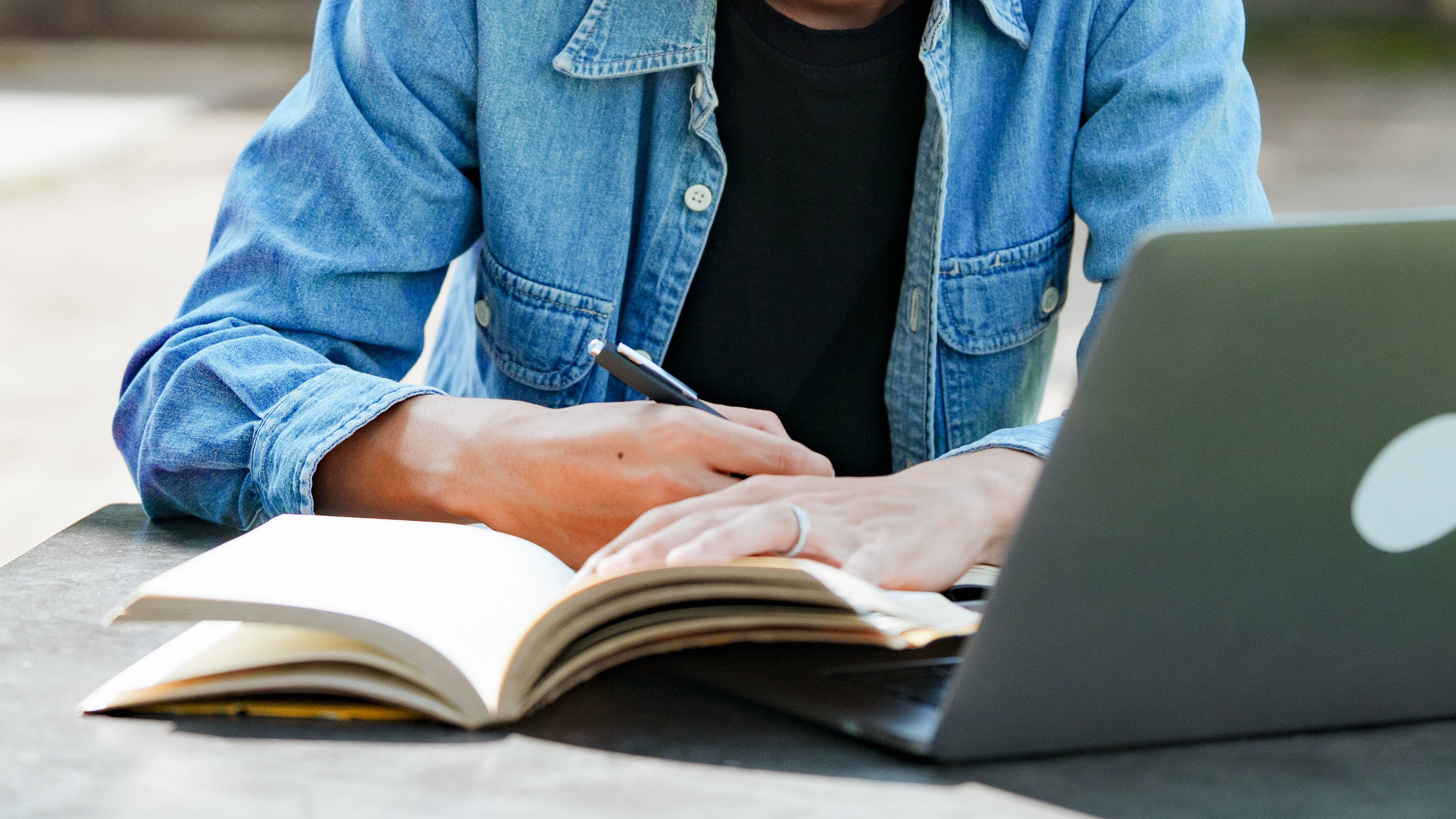 Student beim E-Learning mit einem Laptop auf einer Bank auf dem Campus.