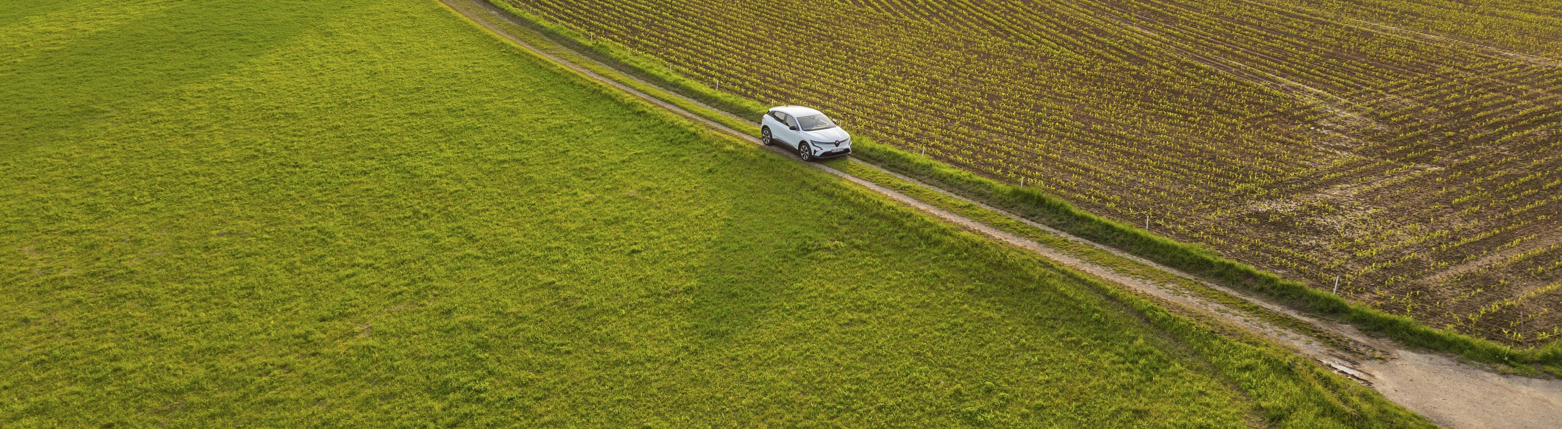 Ein E-Auto fährt auf einem Feldweg durch eine Wiesenlandschaft. Im Bild sieht man das E-Auto von oben.