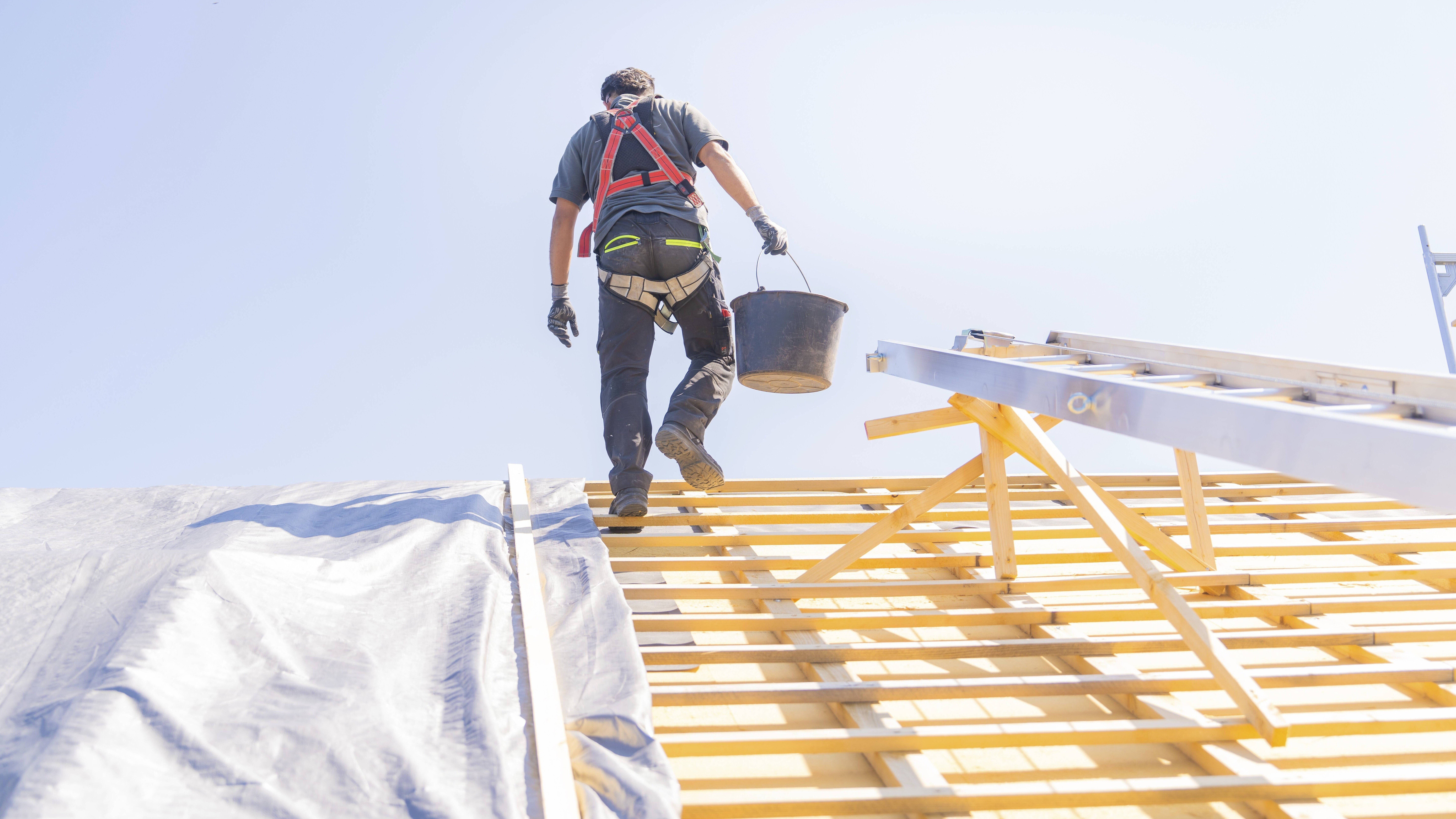 Ein Arbeiter in Sicherheitskleidung klettert eine Leiter hoch, um auf einem Dach zu arbeiten, bei sonnigem Wetter,