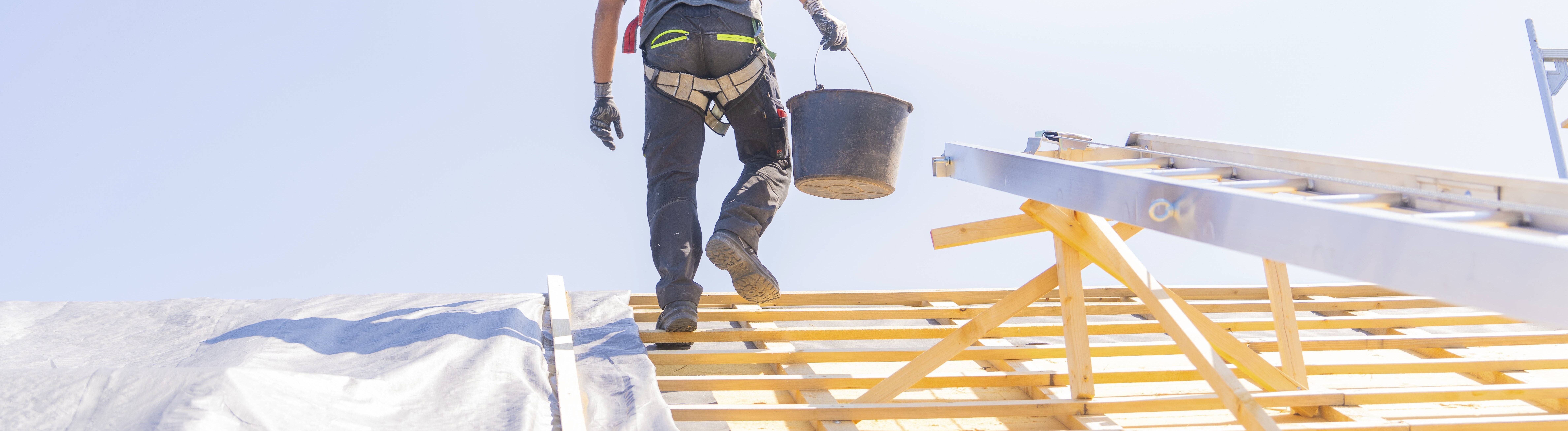 Ein Arbeiter in Sicherheitskleidung klettert eine Leiter hoch, um auf einem Dach zu arbeiten, bei sonnigem Wetter,