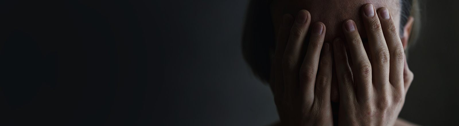 Foto des Kopfes einer Frau, die beide Hände vor ihr Gesicht hält