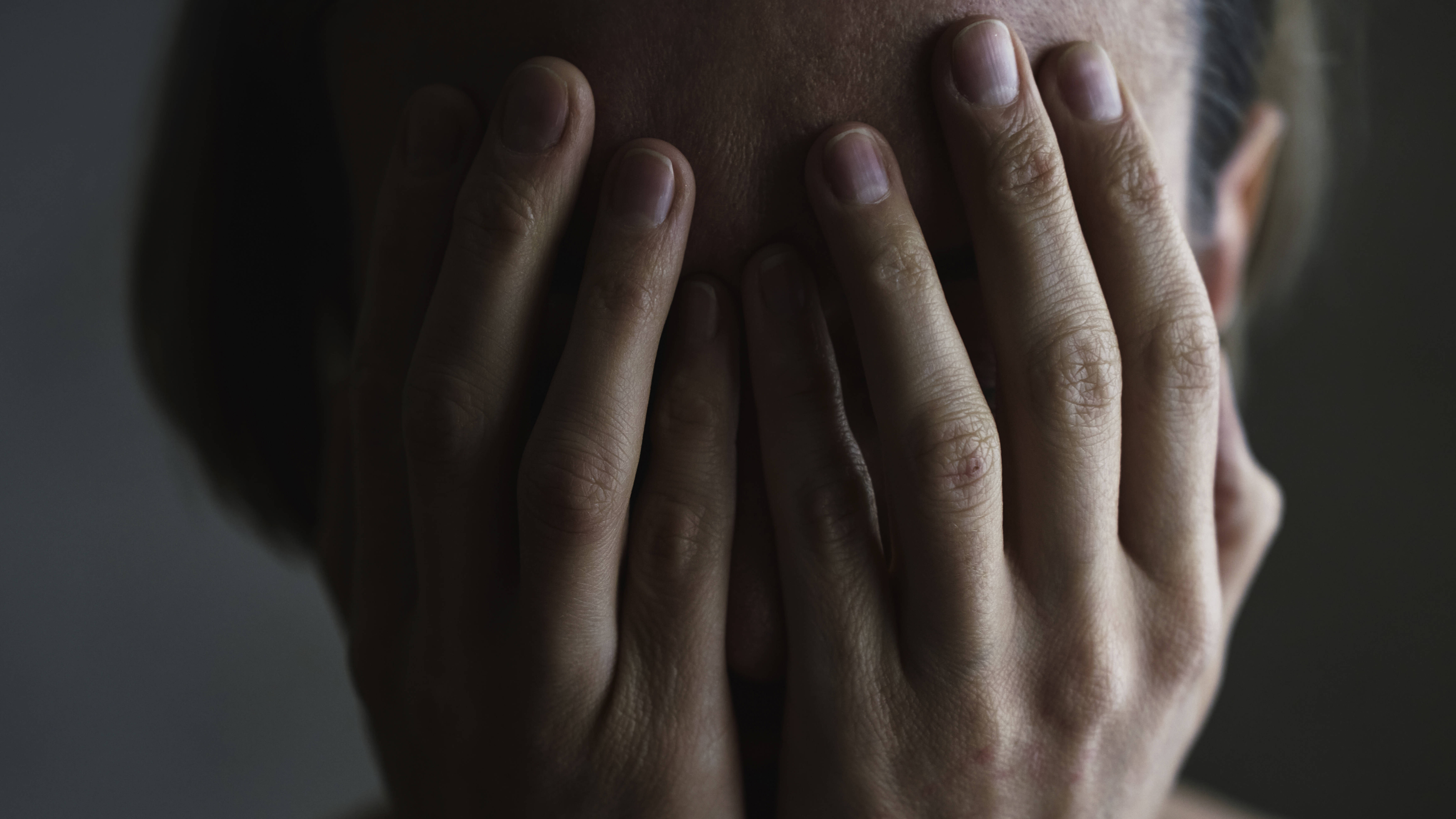 Foto des Kopfes einer Frau, die beide Hände vor ihr Gesicht hält