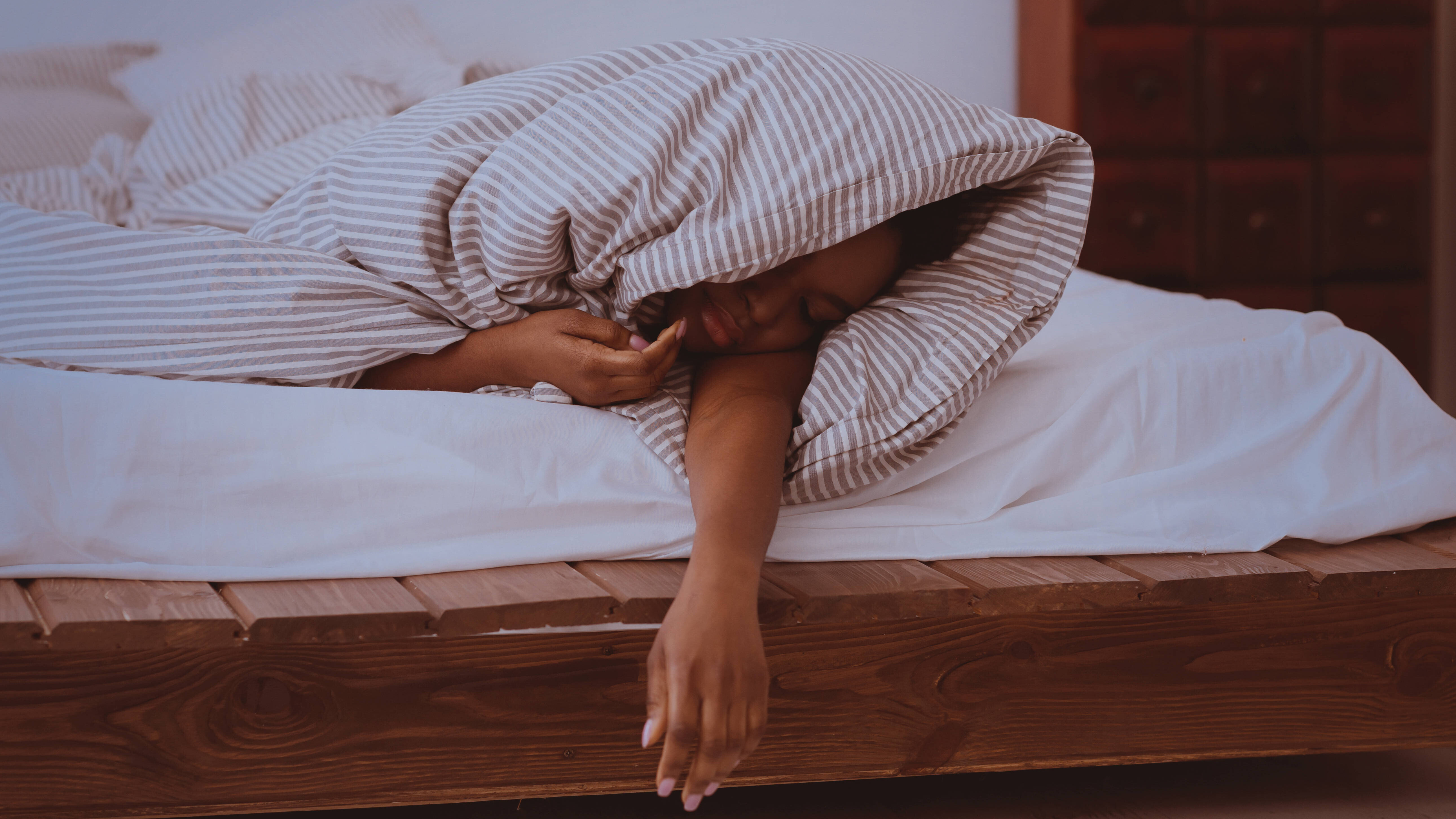 Eine Frau schläft in eine Decke gehüllt auf dem Bett in ihrem Schlafzimmer