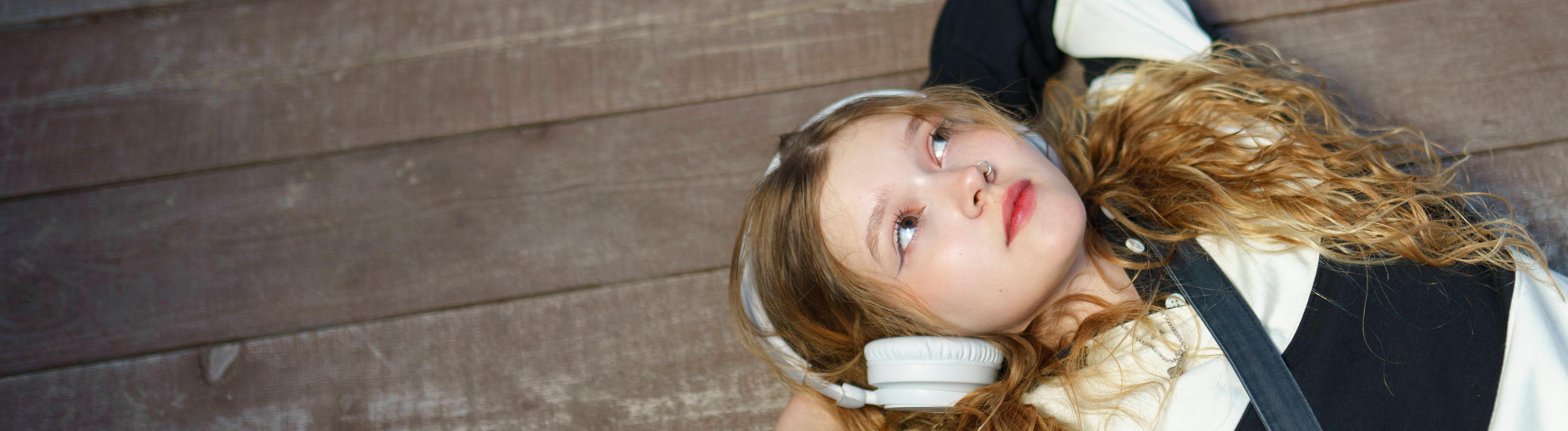 Eine Frau liegt auf dem Boden mit Kopfhörern, der Blick schweift in die Ferne.