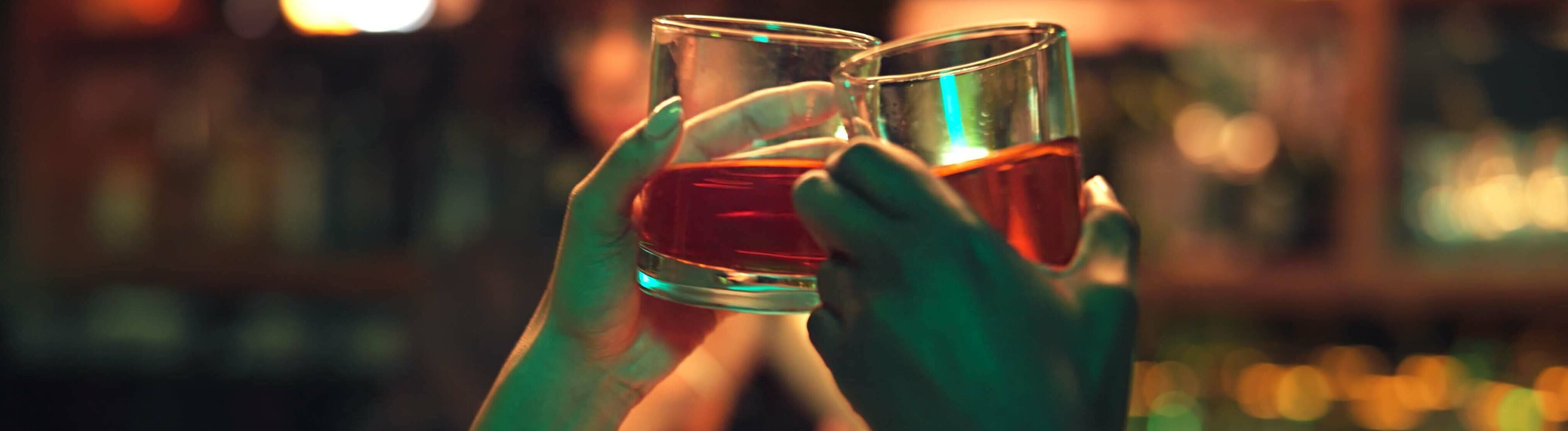 Zwei Personen stoßen mit einem Getränk in einer Bar an