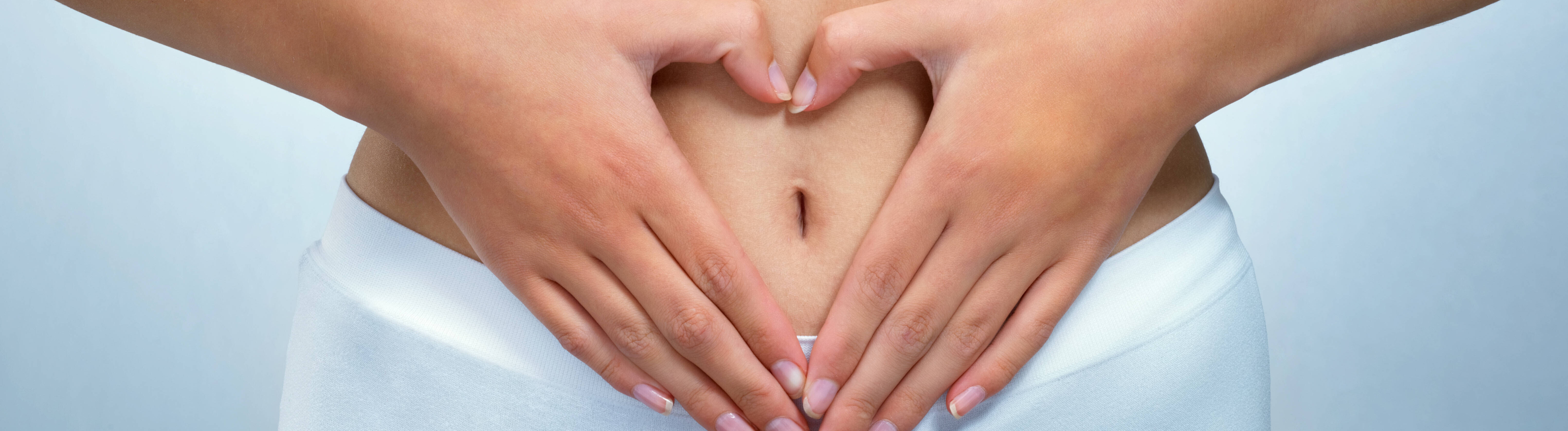 Eine Frau formt mit ihren Händen ein Herz über ihrem Bauch und Unterleib