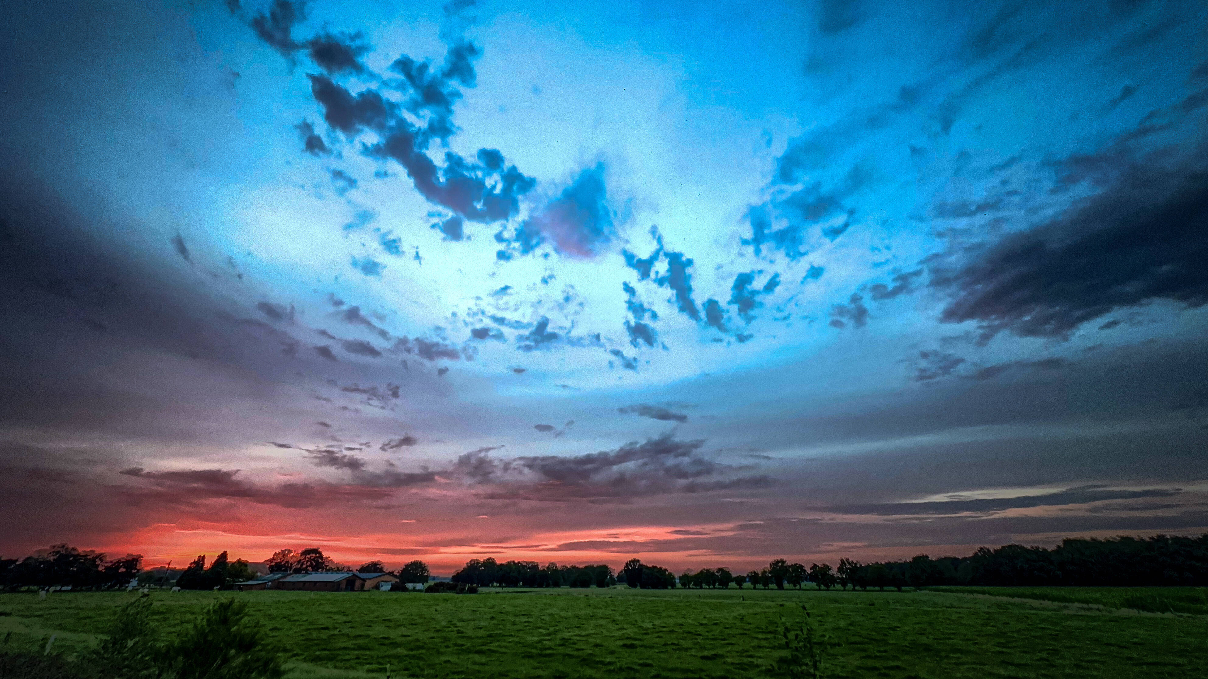 Ein dramatischer Sonnenuntergang über den wogenden Feldern mit wunderschön lebendigem und farbenfrohem Himmel