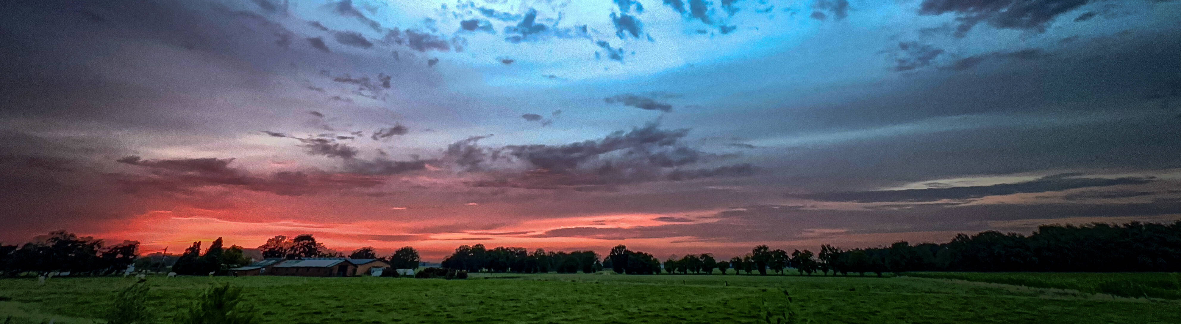 Ein dramatischer Sonnenuntergang über den wogenden Feldern mit wunderschön lebendigem und farbenfrohem Himmel