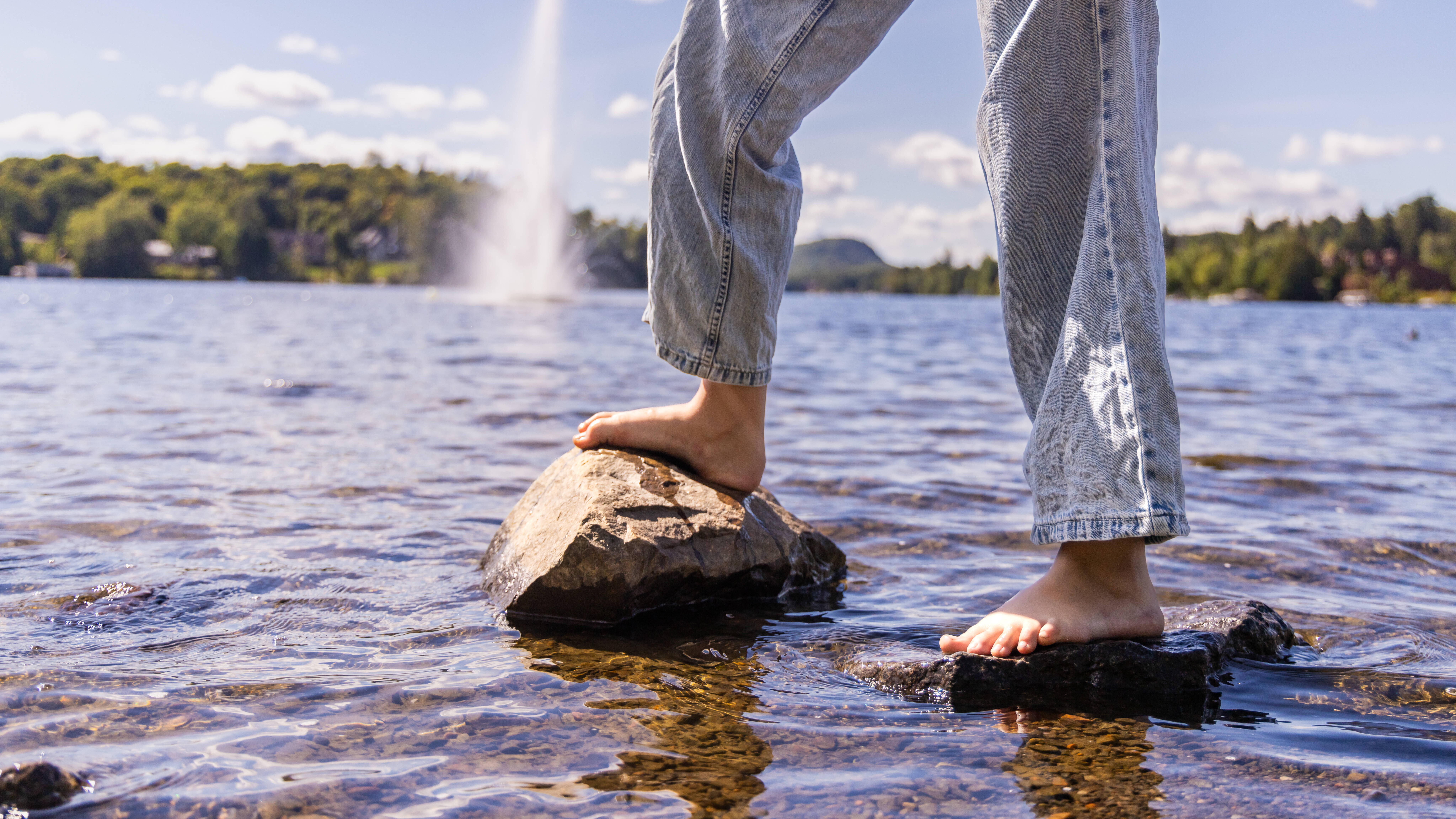 Junge Frau balanciert auf Felsen in einem See mit Springbrunnen im Hintergrund