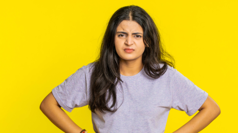 Eine irritierte Frau mit braunen langen Haaren stemmt die Hände in die Seiten