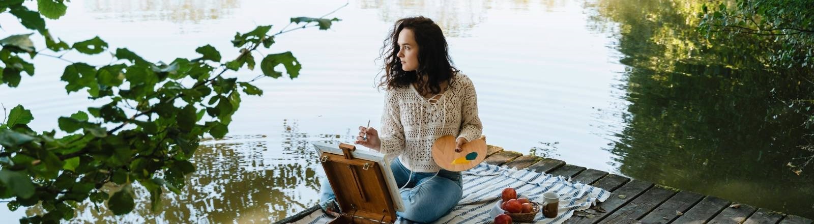 Eine Frau sitzt an einem See und malt