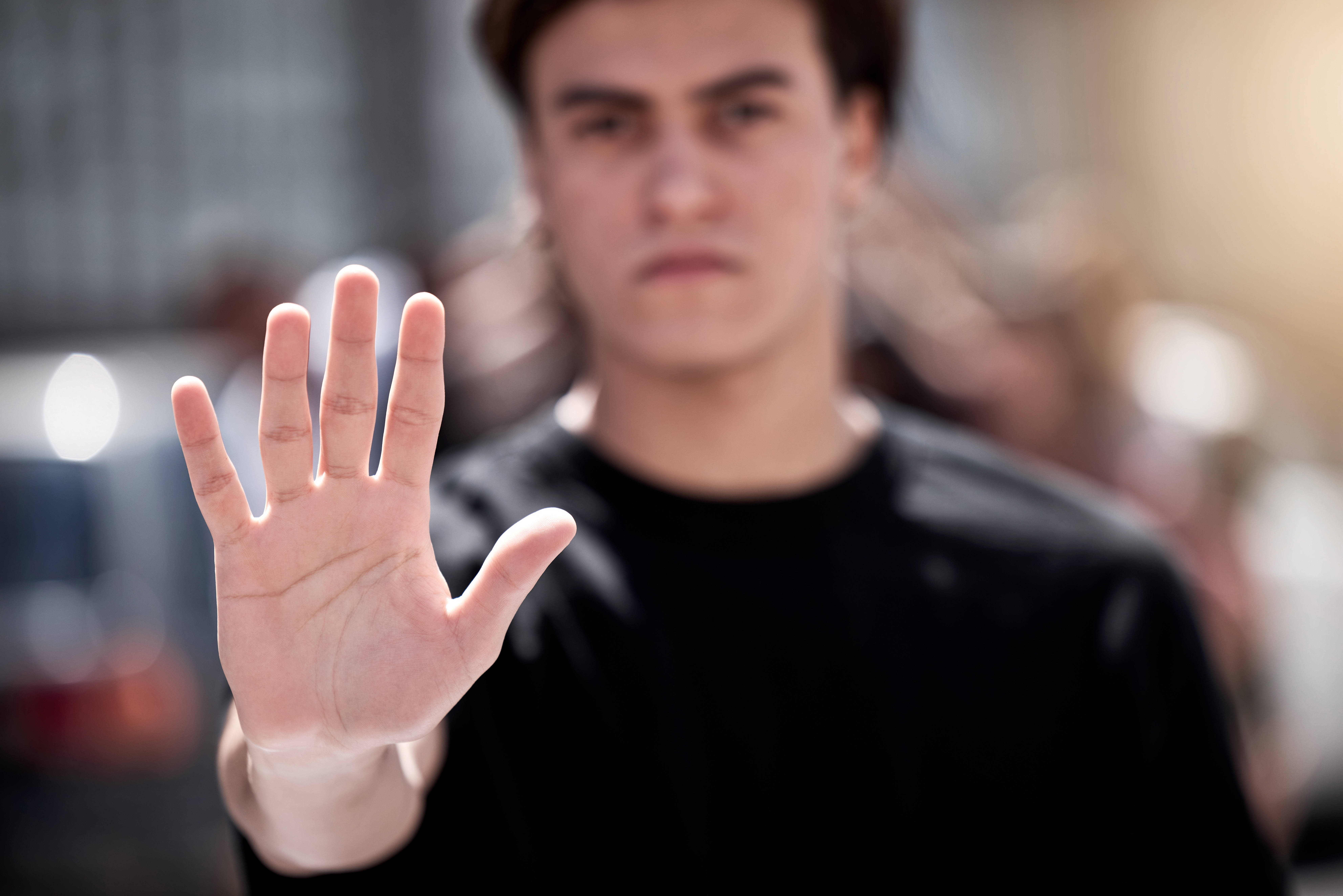 Foto eines jungen Mannes, der die Hand hebt und so "Stopp" signalisiert - Die Hand vorne ist scharf, der Mann dahinter unscharf.