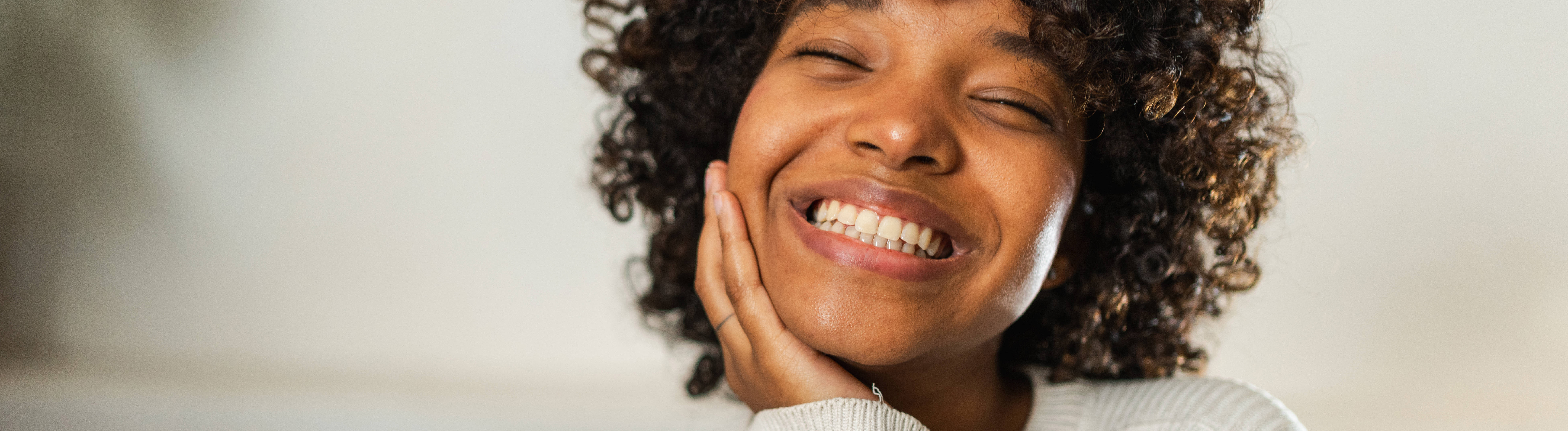 Eine Frau mit geschlossenen Augen lacht und hat das Kinn auf die Hand gestützt.