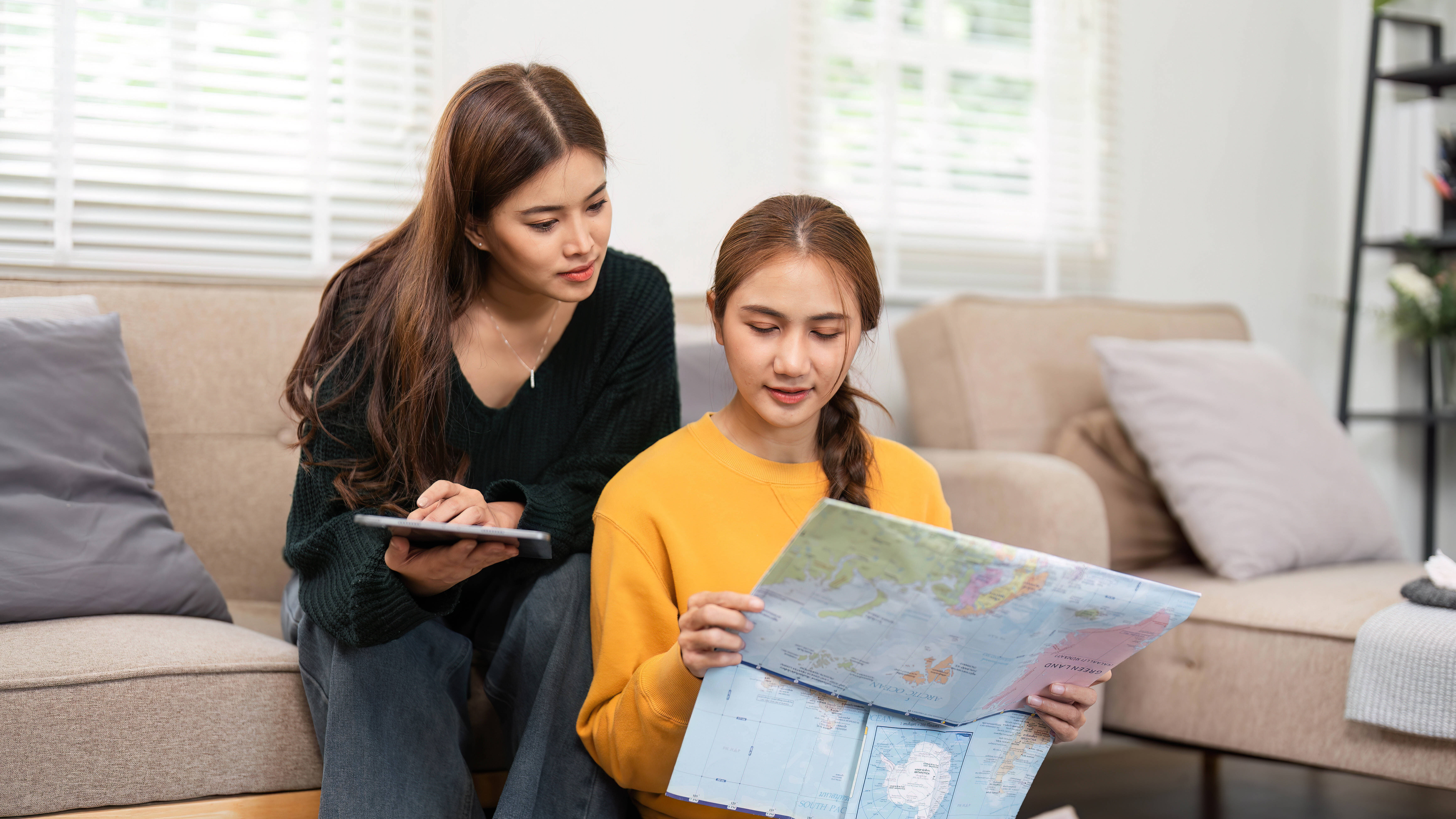 Zwei Frauen schauen auf ein Tablet und eine Landkarte