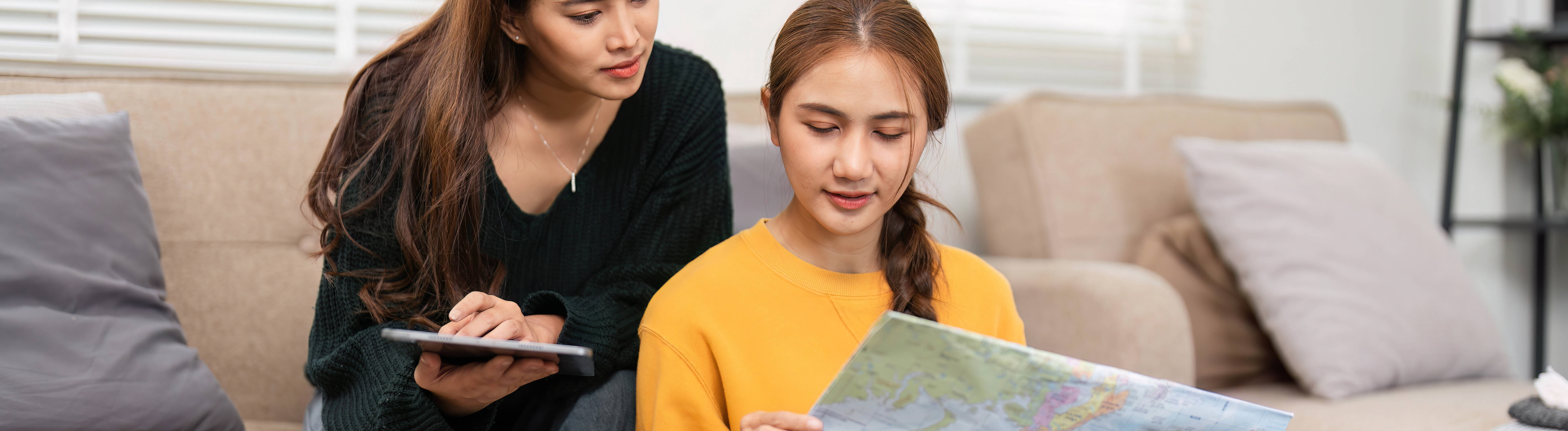 Zwei Frauen schauen auf ein Tablet und eine Landkarte