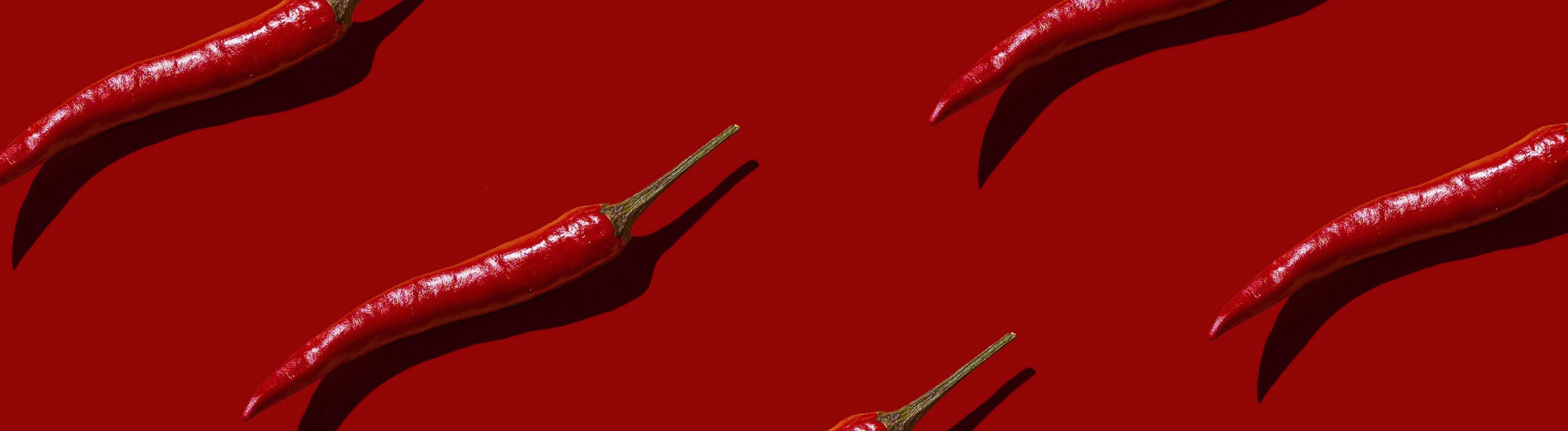 Auf einem roten Hintergrund liegen mehrere einzelne Chilischoten.