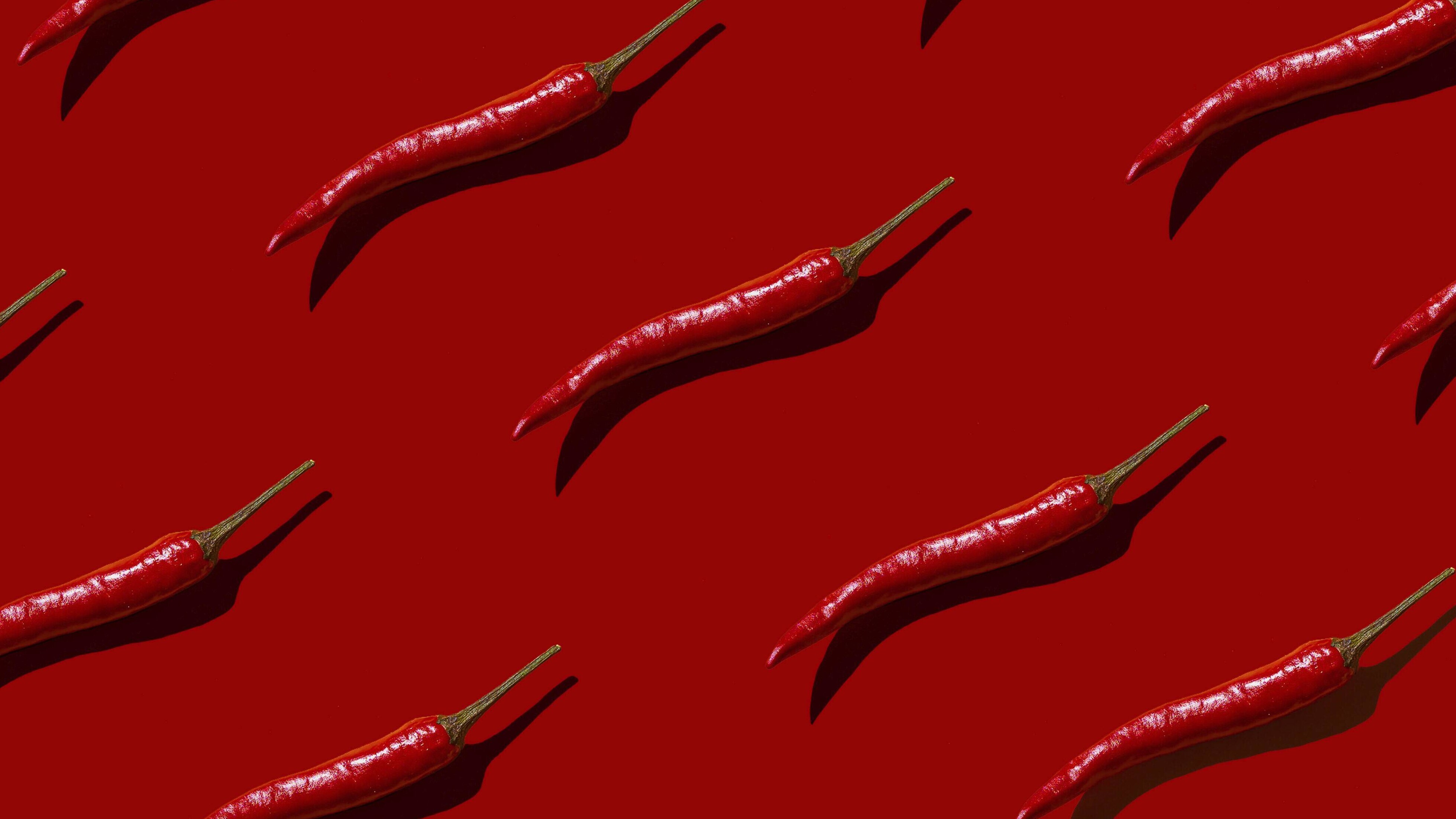 Auf einem roten Hintergrund liegen mehrere einzelne Chilischoten.