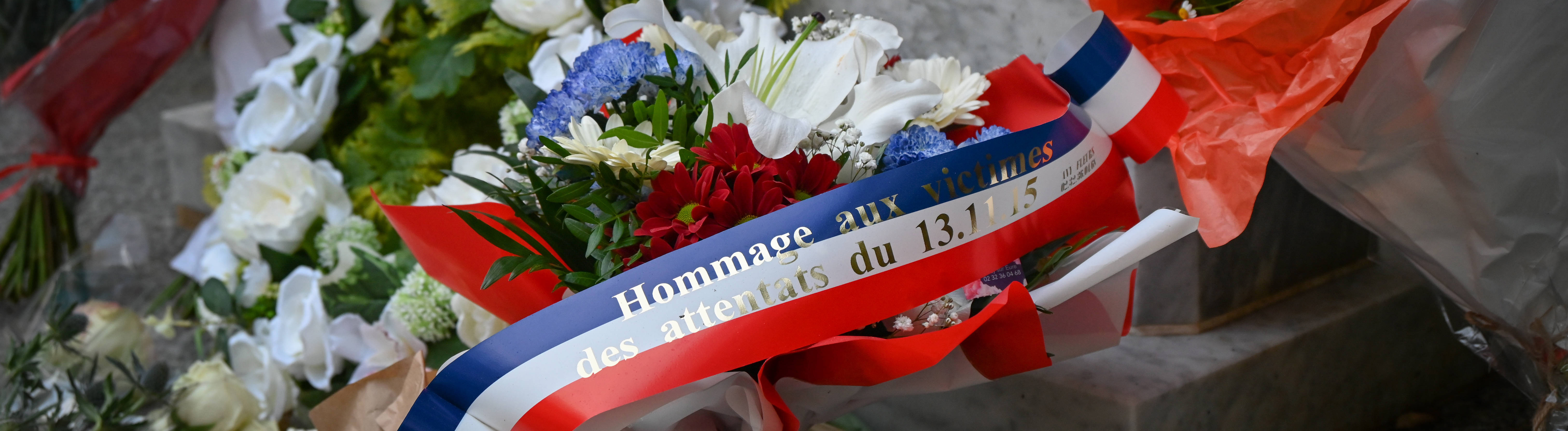 Ein Blumengesteck mit einer Schleife in den Farben der französischen Nationalflagge, auf dem steht: "Hommage an die Opfer der Anschläge vom 13. November 2015".