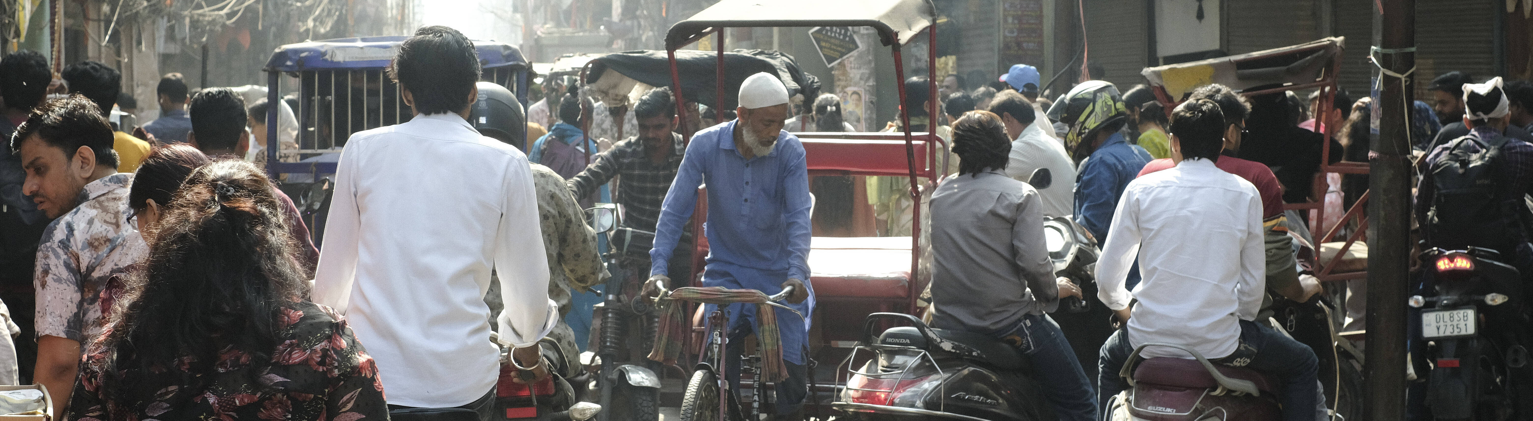 Eine Straßenszene in Neu Delhi: Menschen und eine Rikscha tummeln sich auf der Straße