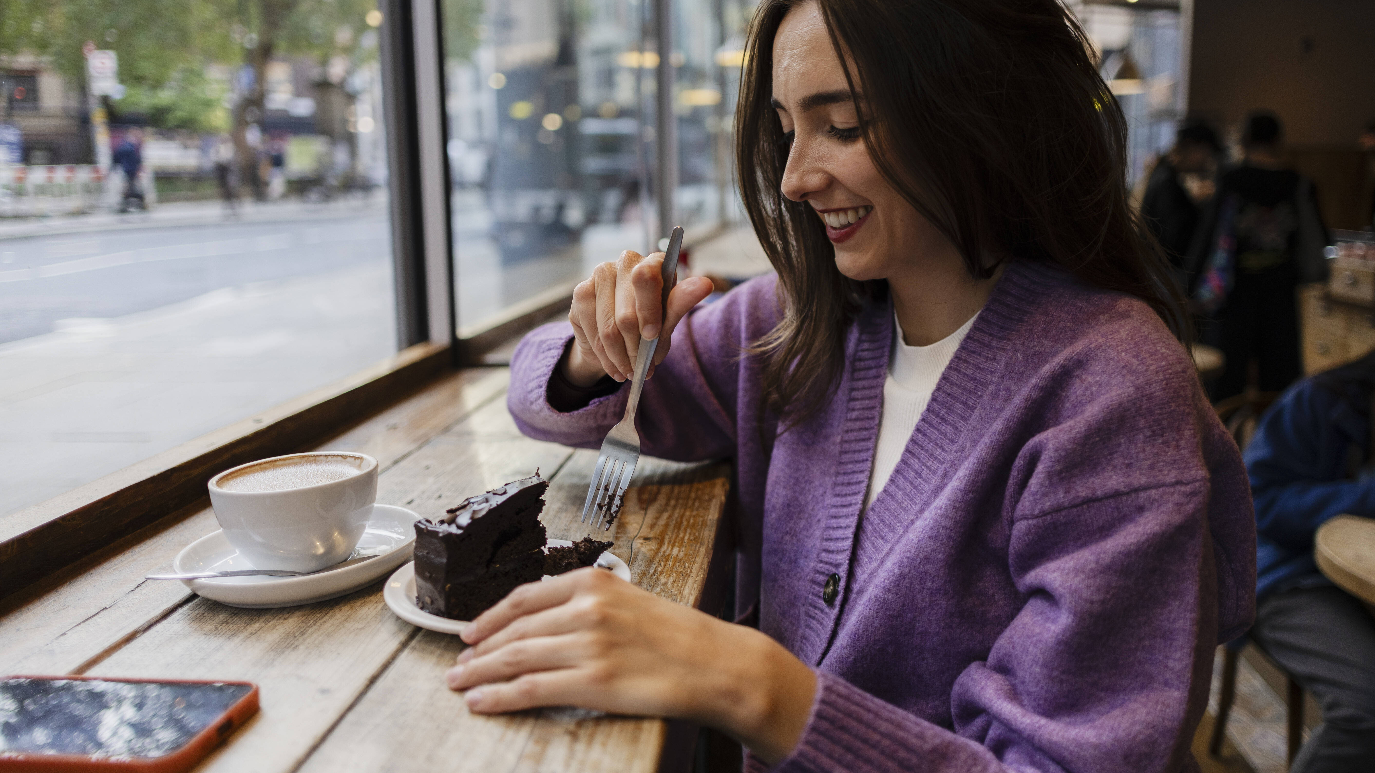Eine Frau trinkt alleine Kaffee und isst Kuchen in einem Café