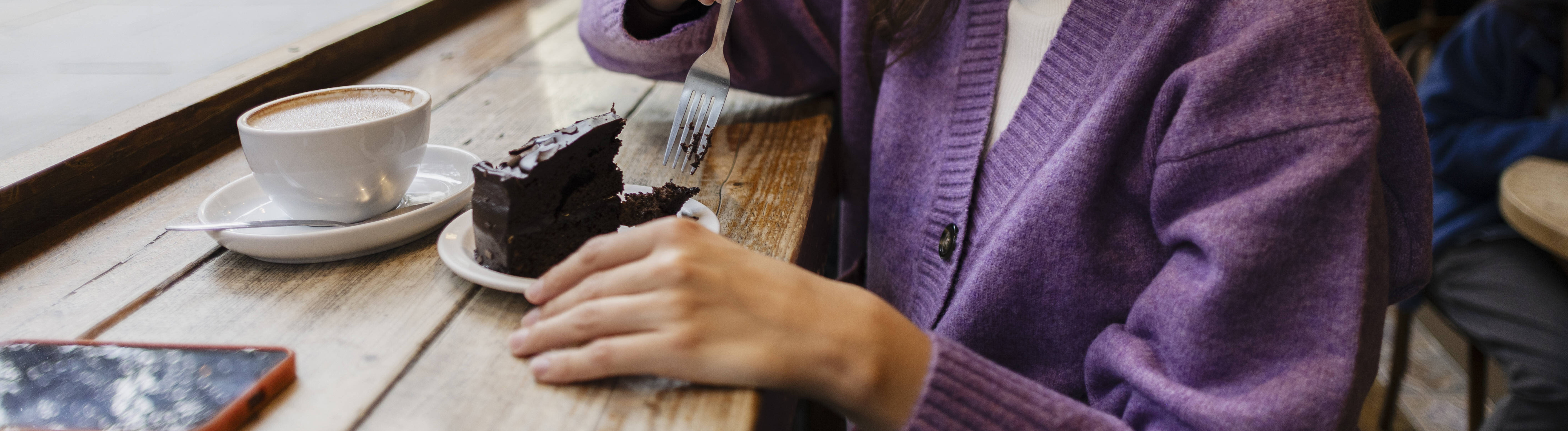 Ein Frau trinkt alleine Kaffee und isst Kuchen in einem Cafe