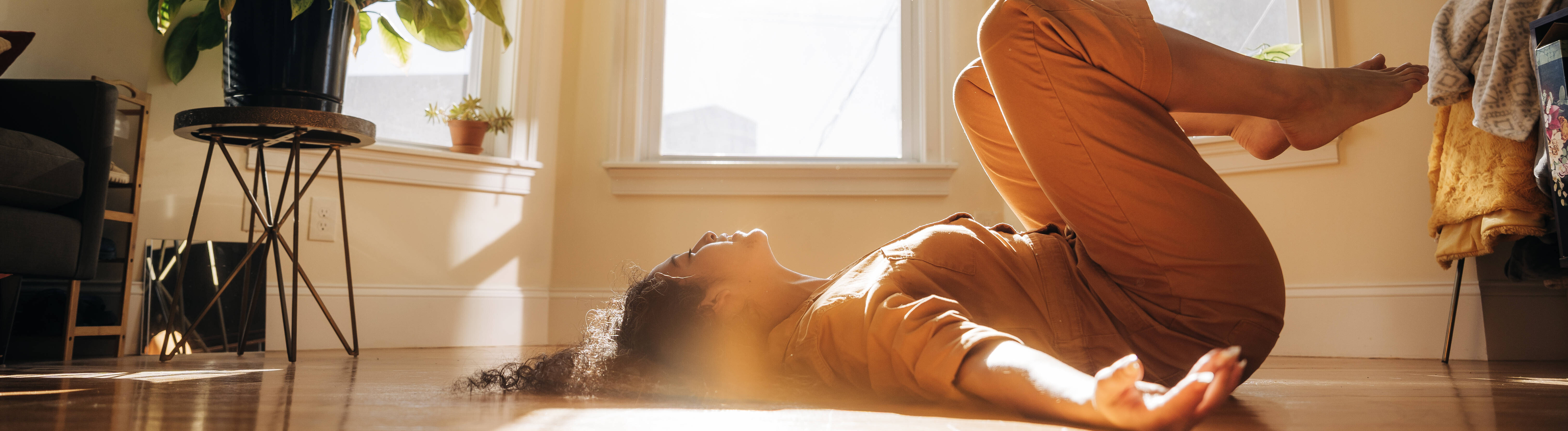 Eine Frau macht in einer sonnendurchfluteten Wohnung eine Yoga-Übung auf dem Boden