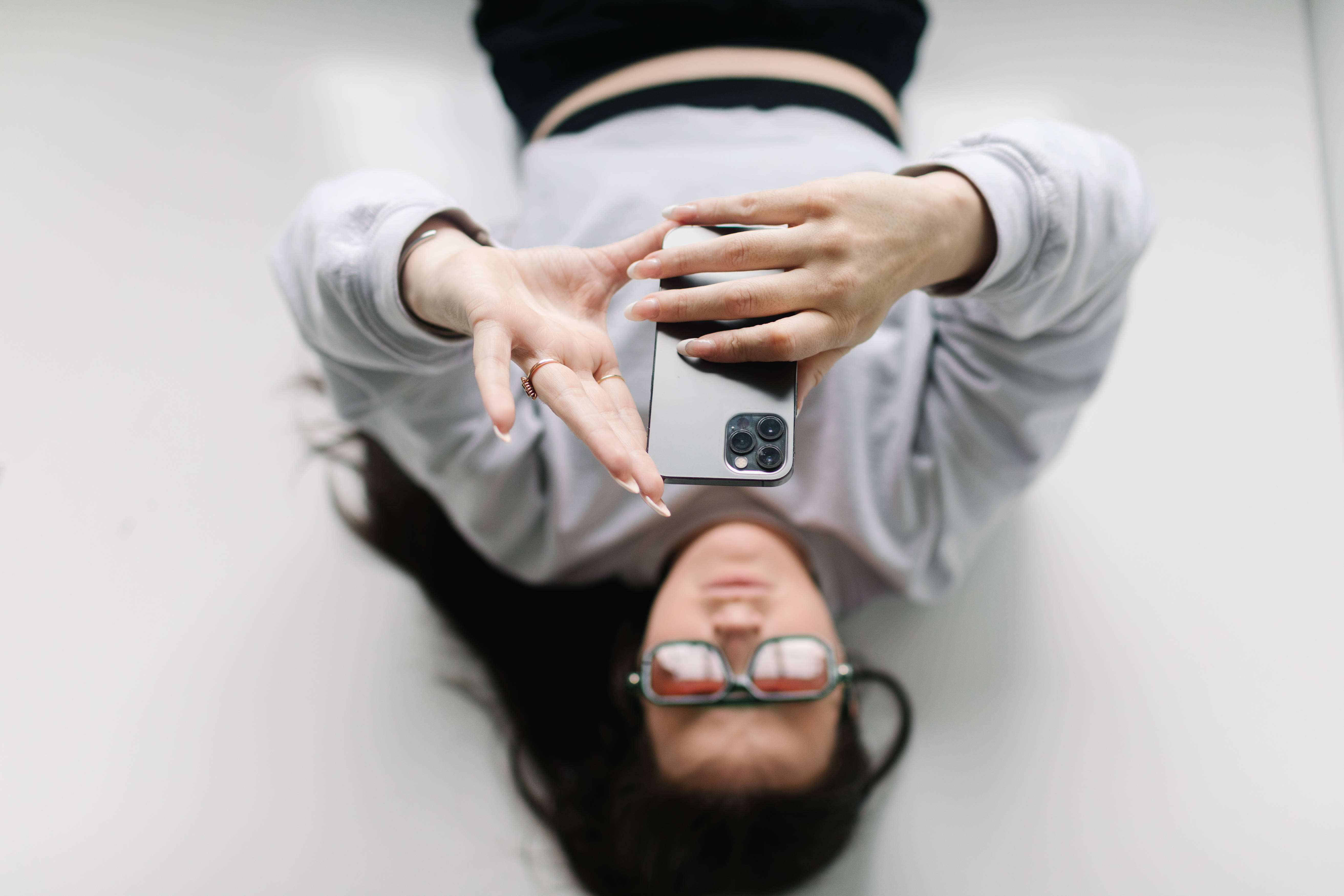 Eine junge Frau liegt auf dem Rücken und tippt auf ihrem Smartphone, das sie über sich hält.